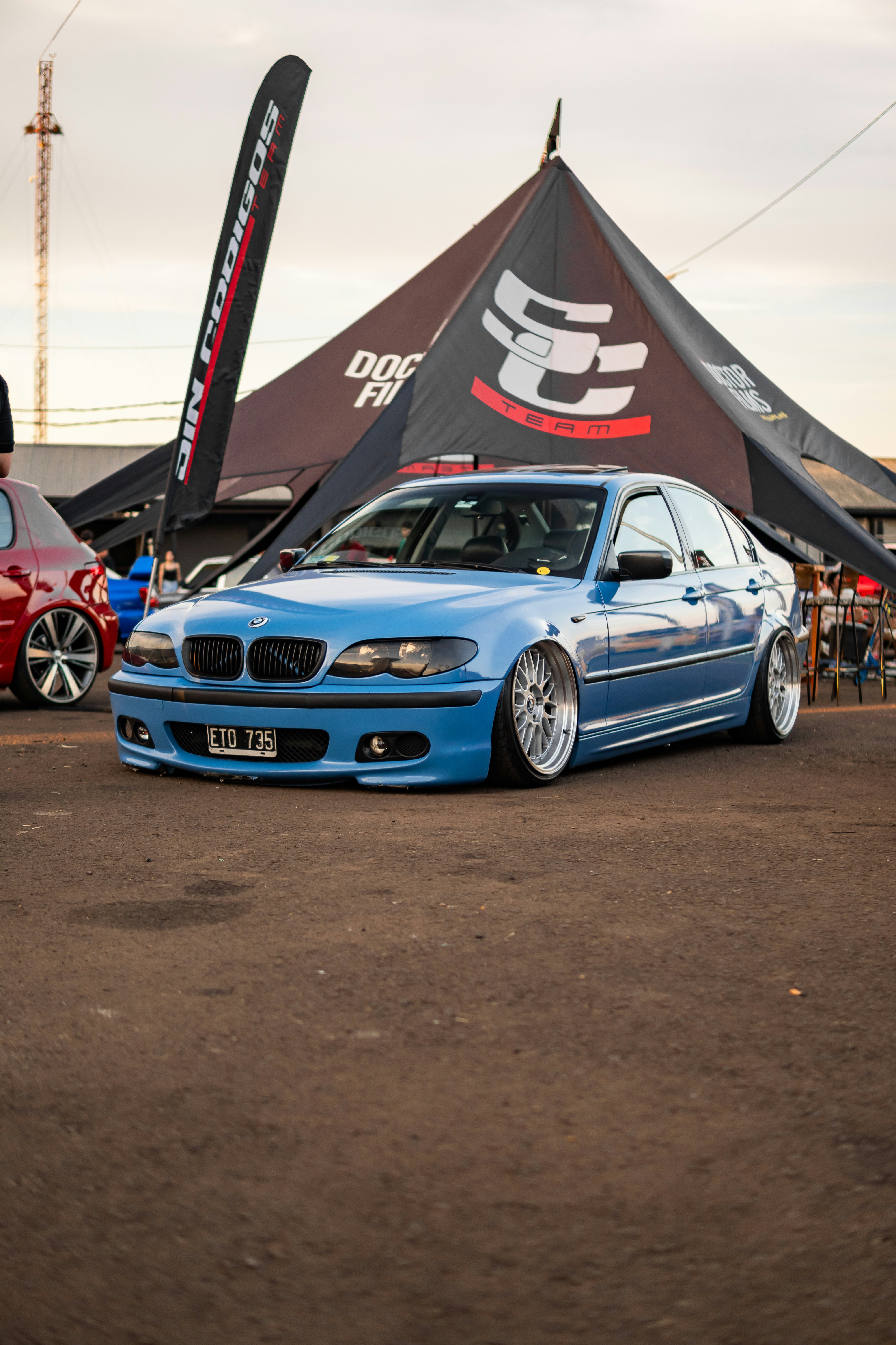 BMW sedã azul modificado com suspensão rebaixada em um evento.