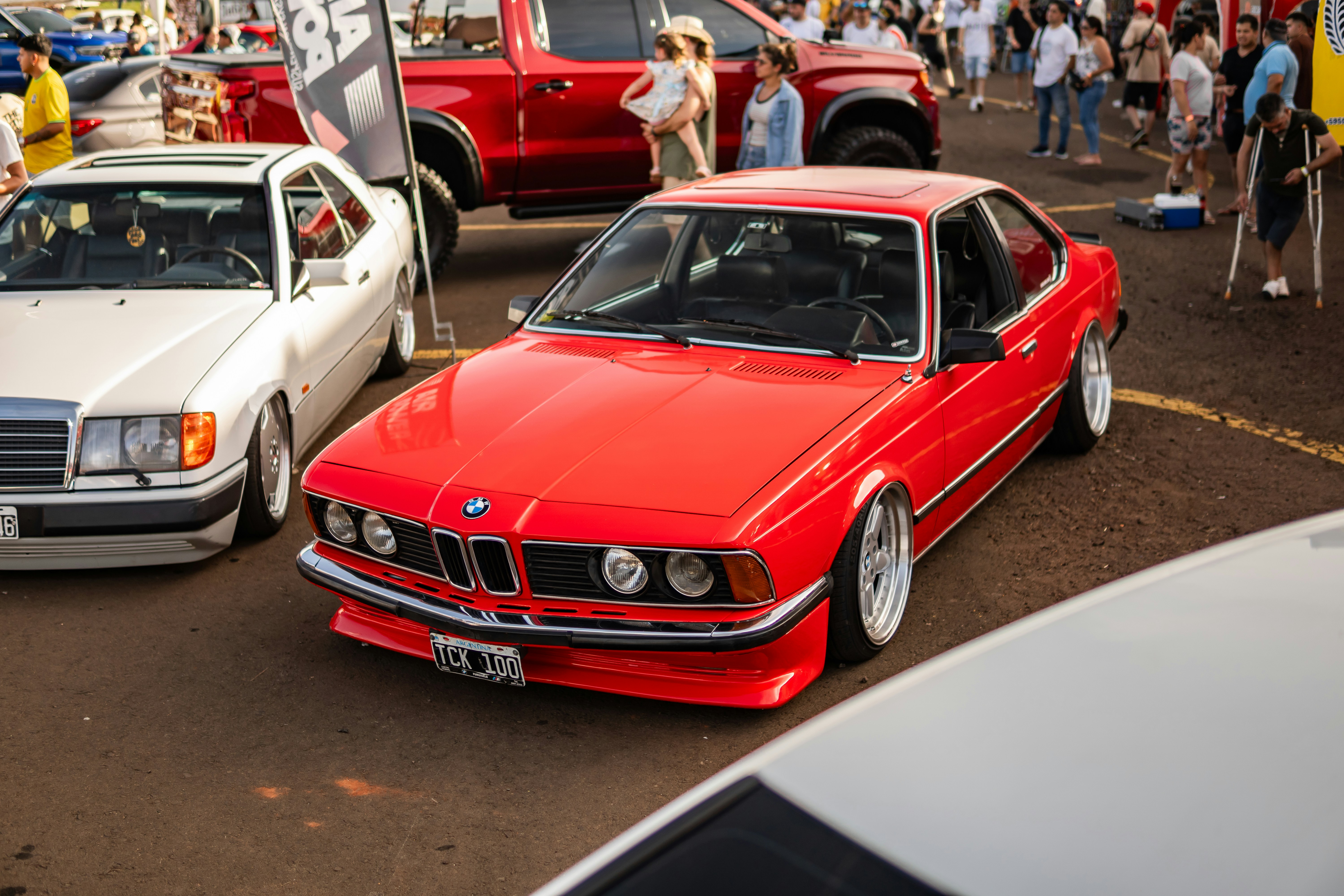 Um cupê BMW vermelho personalizado estacionado entre outros veículos.