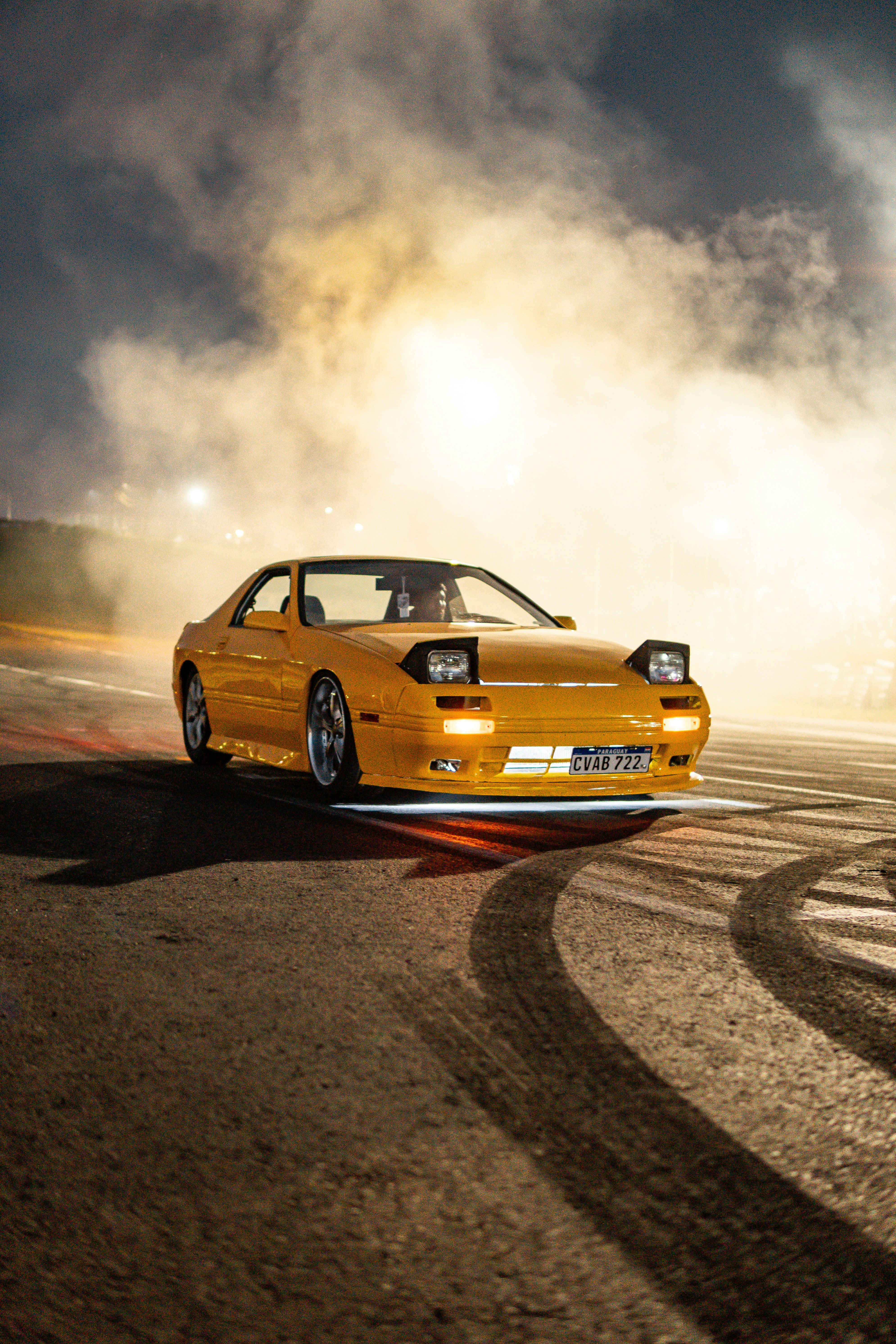 Carro esportivo amarelo derrapando com fumaça e marcas de pneus.