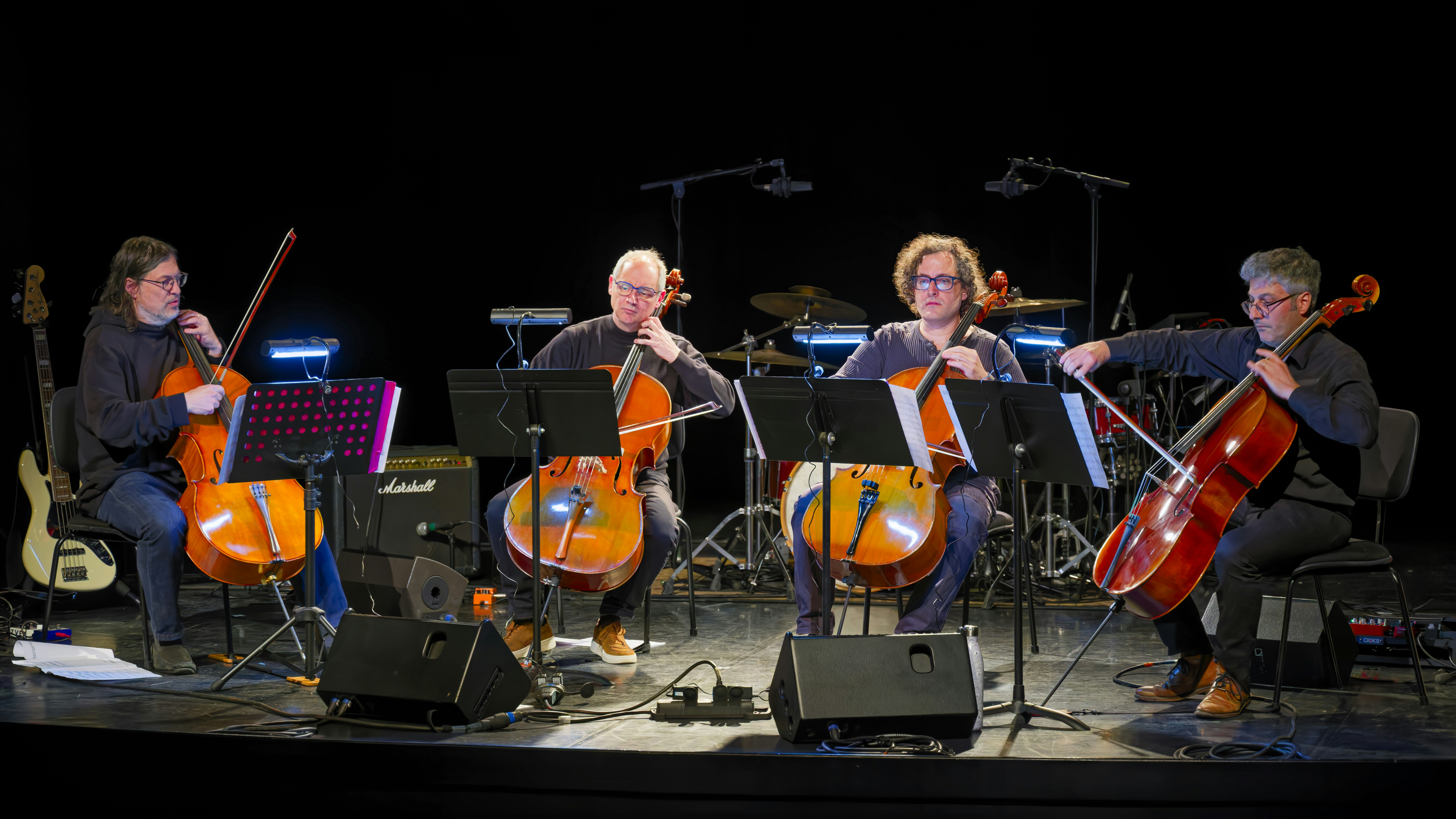 Four musicians playing cellos on a dark stage