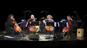 Four musicians perform on cellos on a dark stage