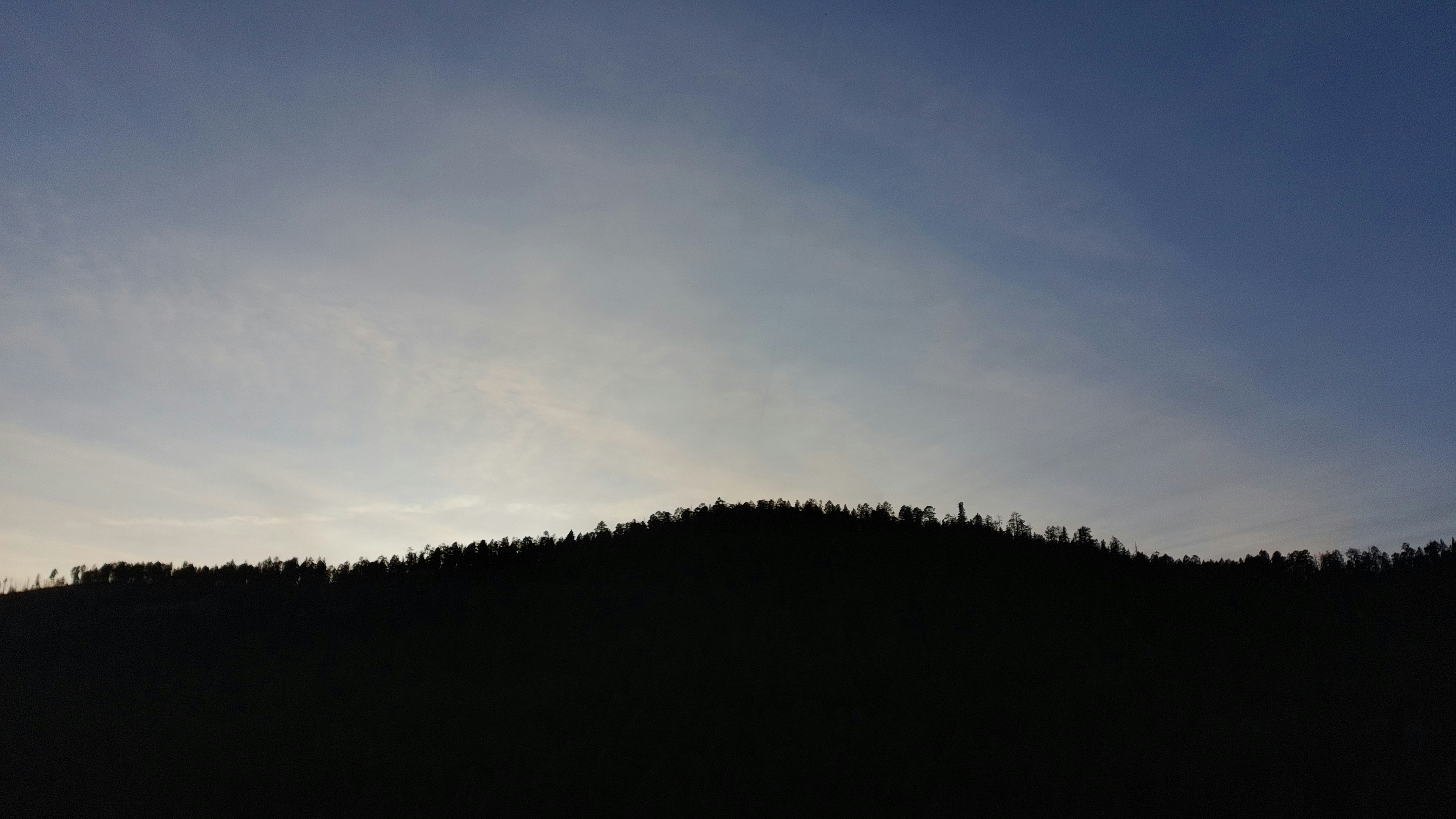 Silhouetted hillside under a softly lit sky, capturing the gradient from the dark ridge to the pale horizon.
