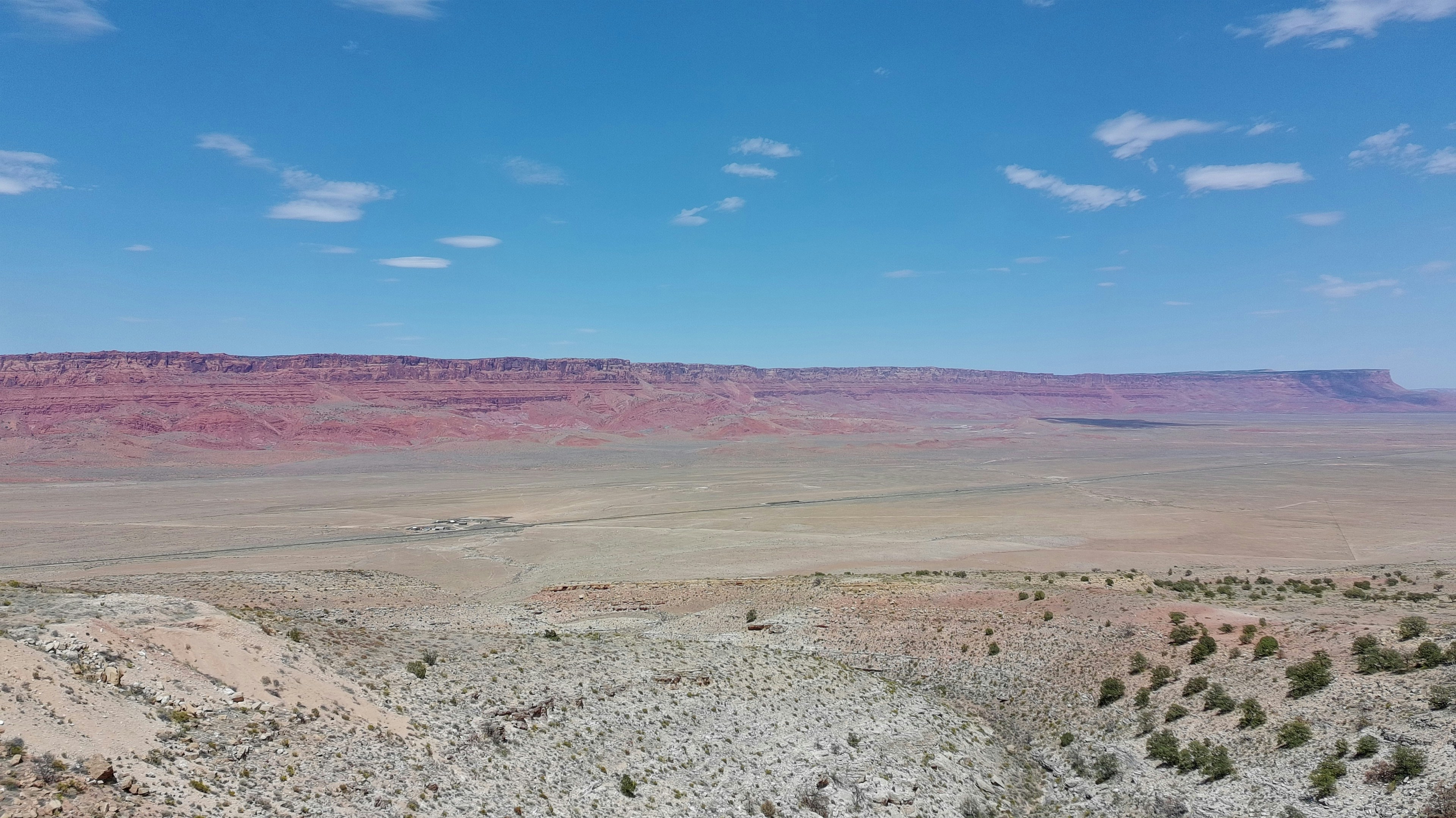 Vast desert landscape with red rock cliffs under blue sky.