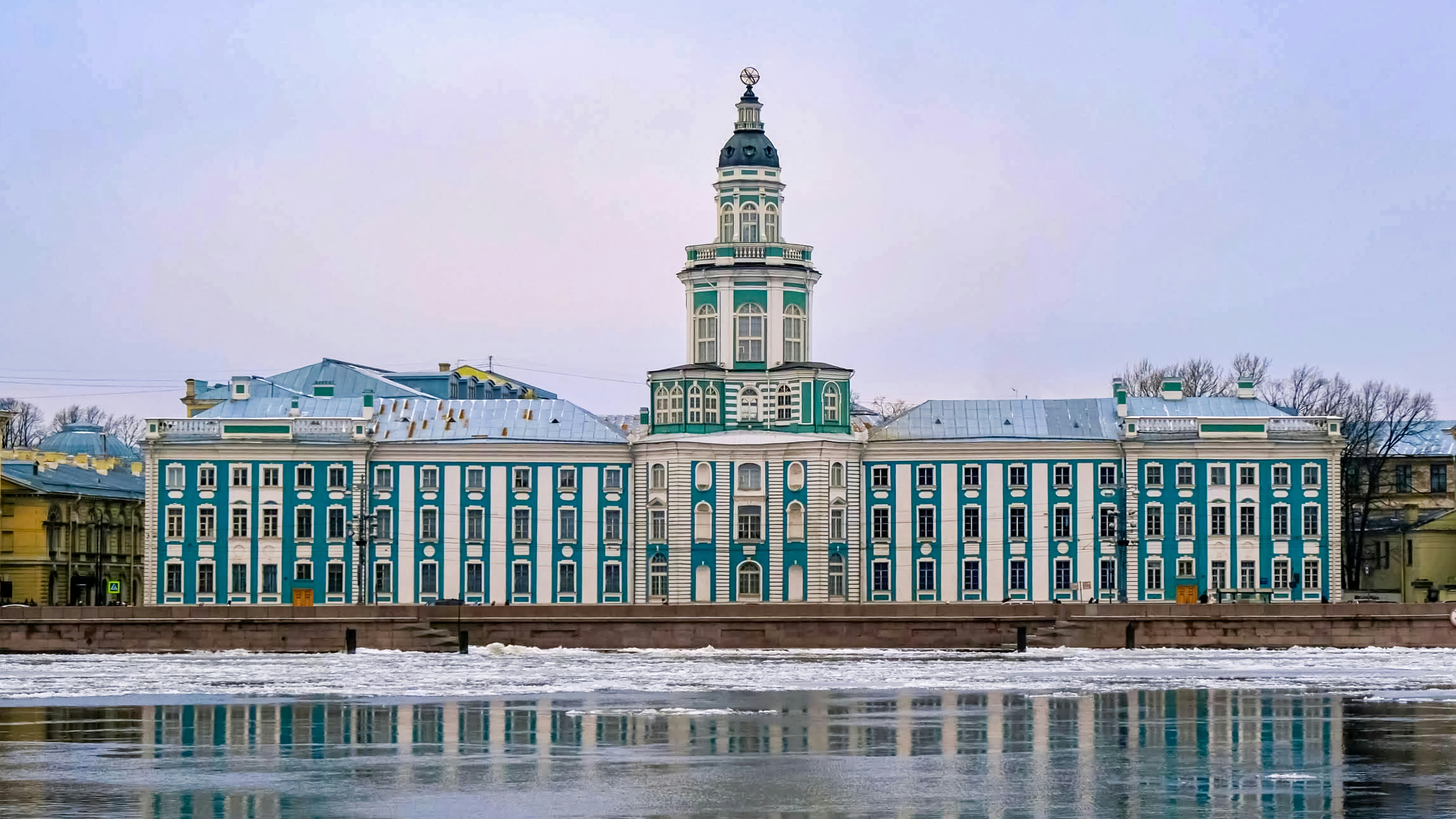 Ornate building with a tower reflected in icy water.