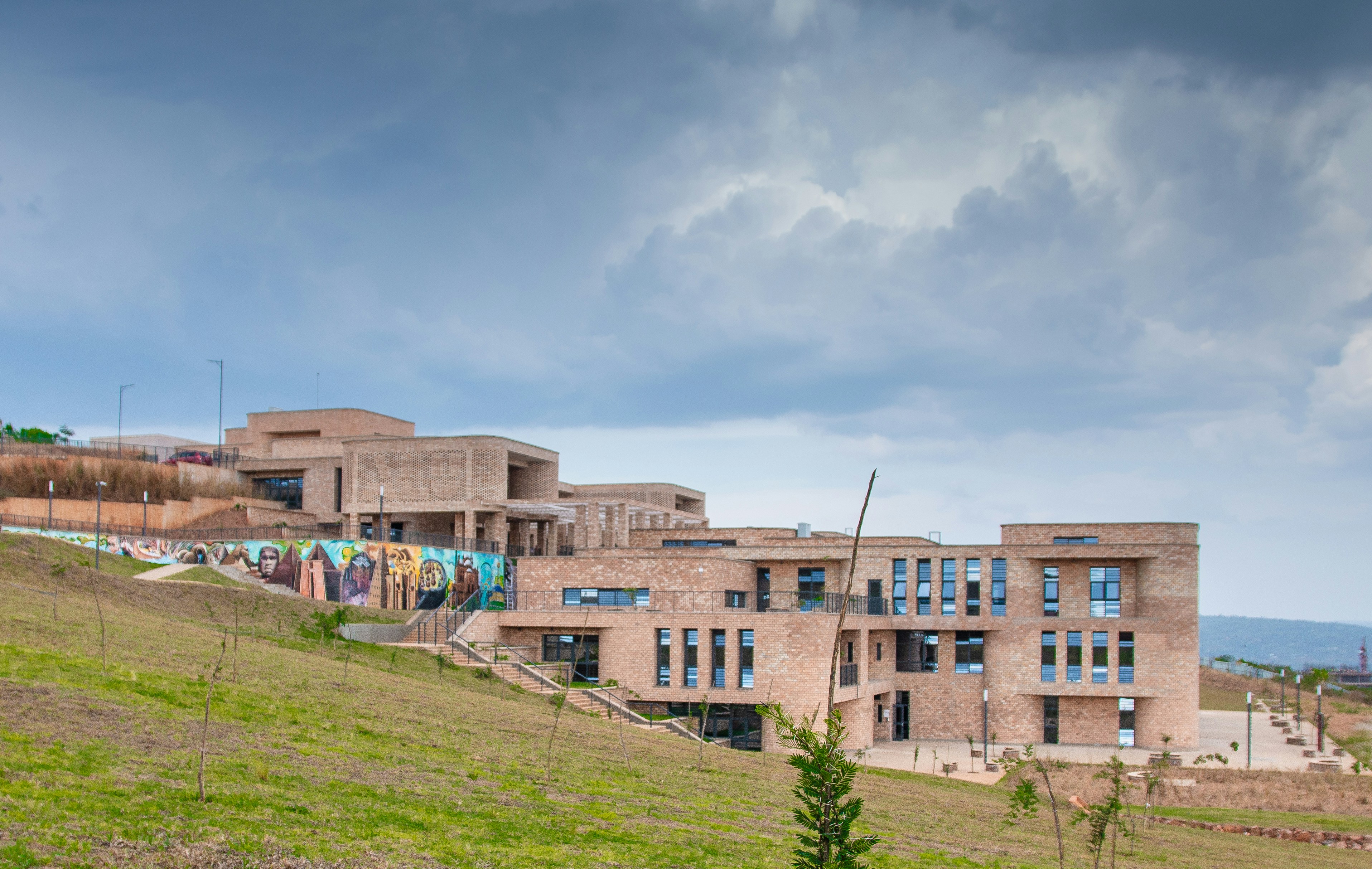 Modern building complex on a green hillside under cloudy sky.