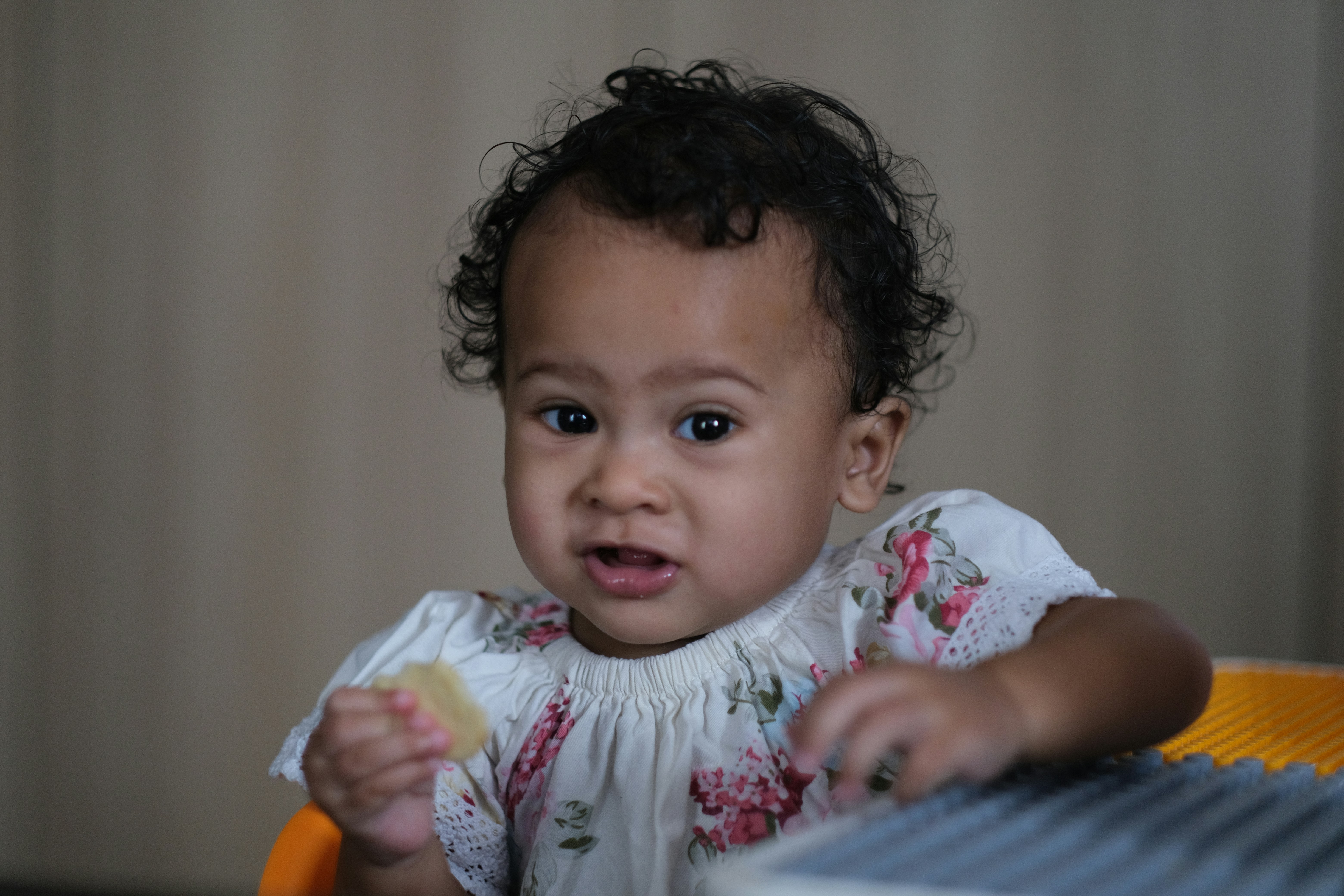 Bayi lucu dengan rambut keriting memegang camilan.