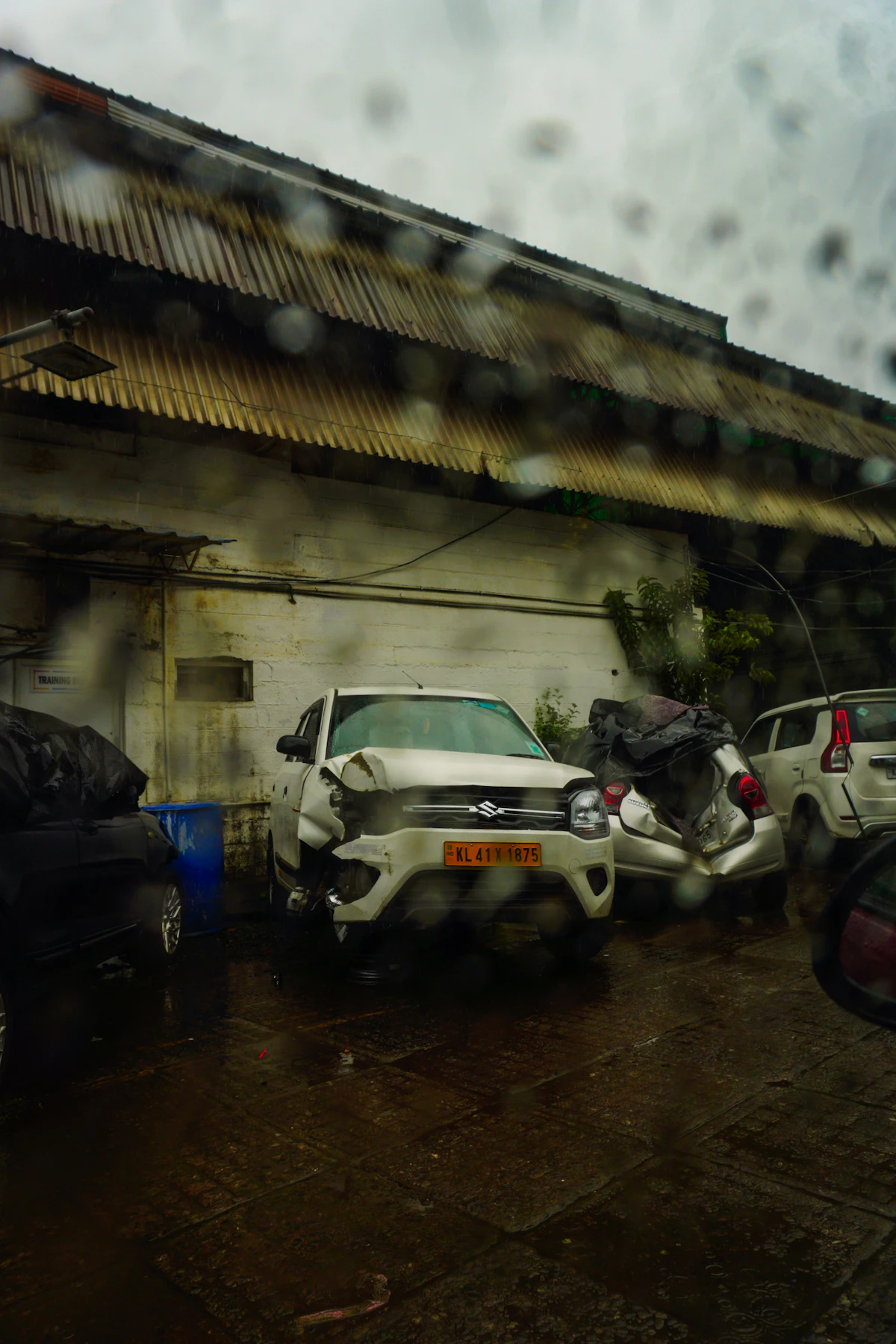 Mobil-mobil rusak terparkir di depan bangunan saat hujan