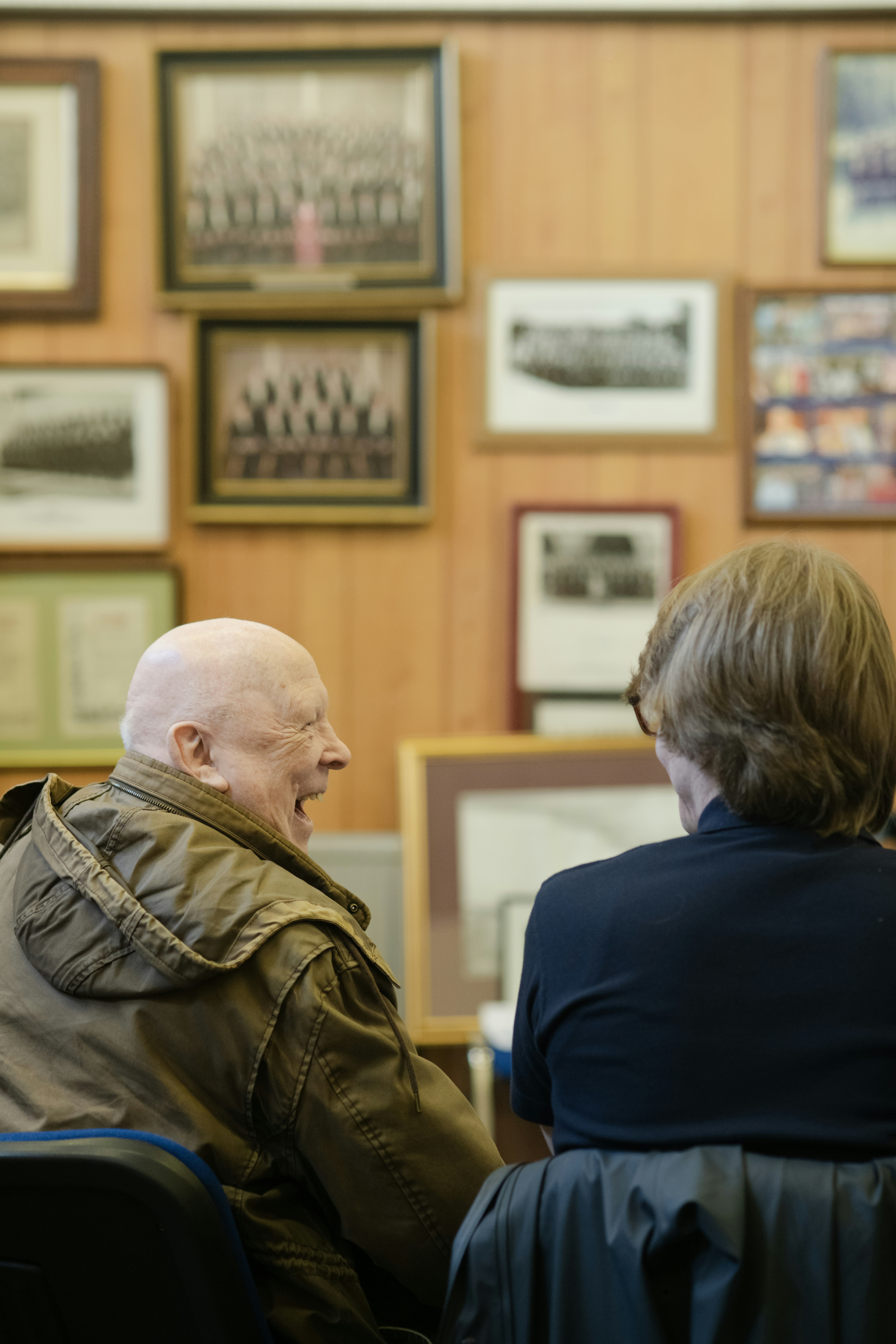 Elderly man laughs while talking to another person.