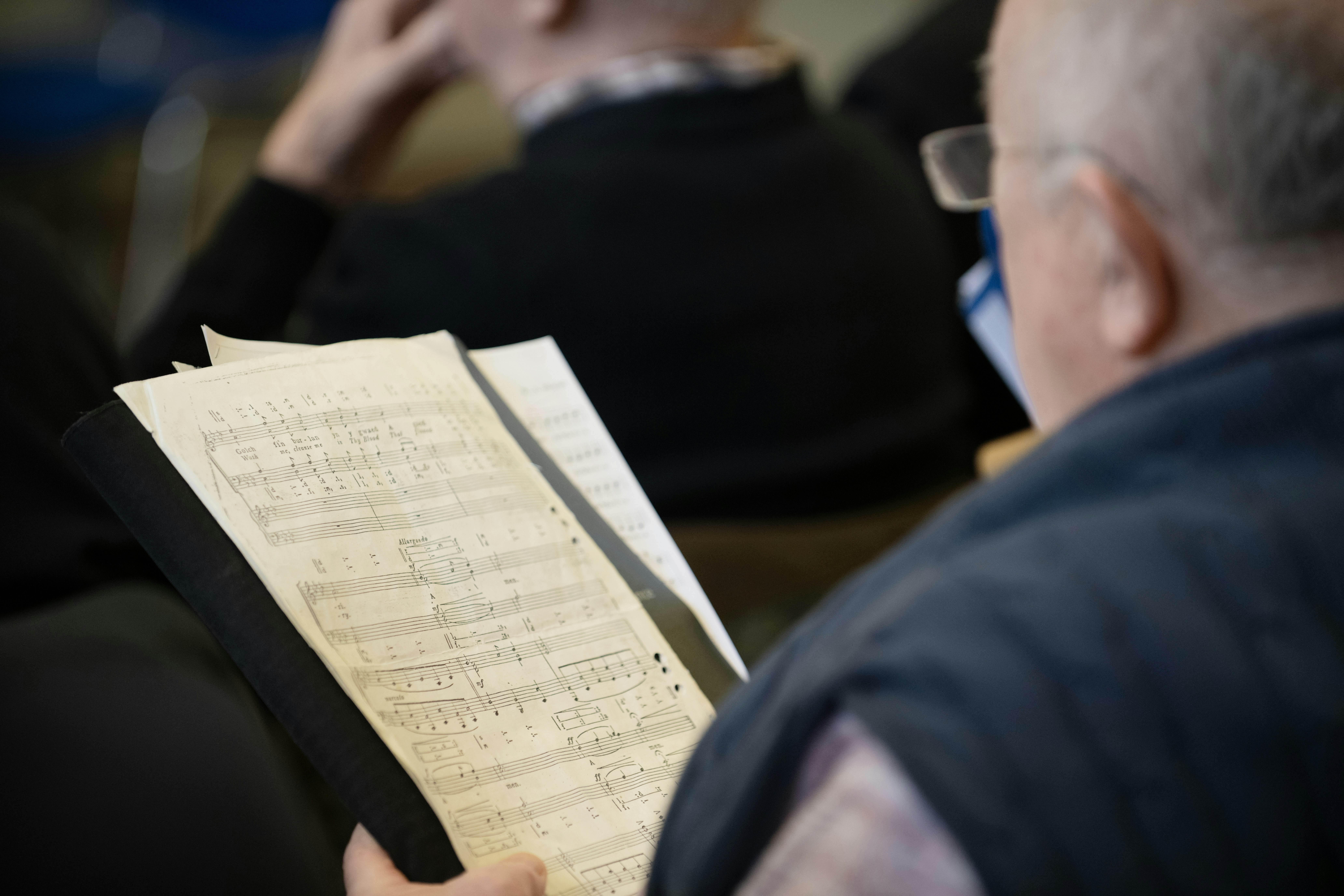 Man in glasses holds sheet music with handwritten musical notes.