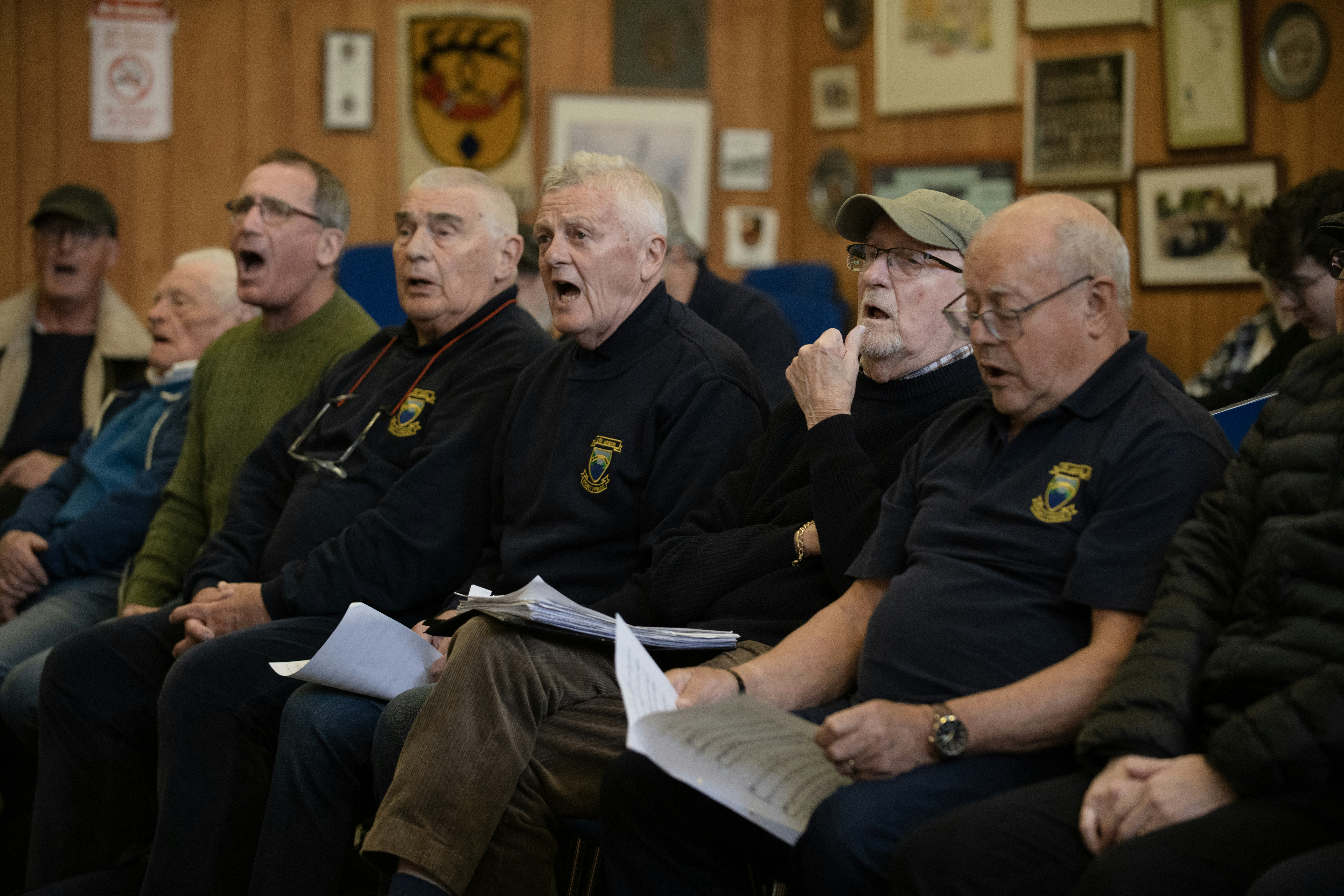 Elderly men sitting and singing together from sheet music.