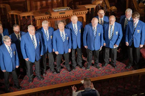 A male choir in blue blazers performs on stage.