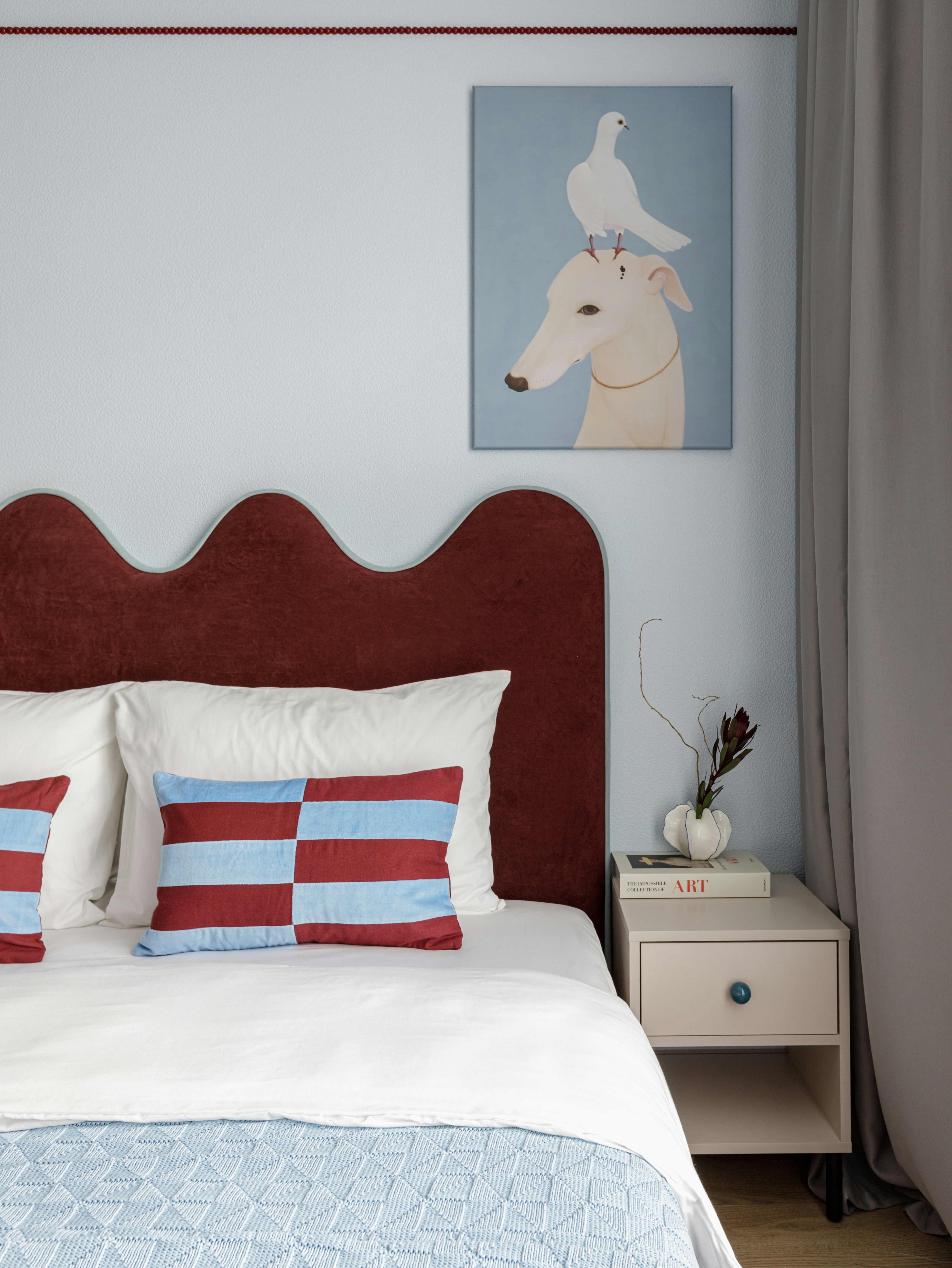 Cozy bedroom with red headboard, striped pillow, and dog painting.