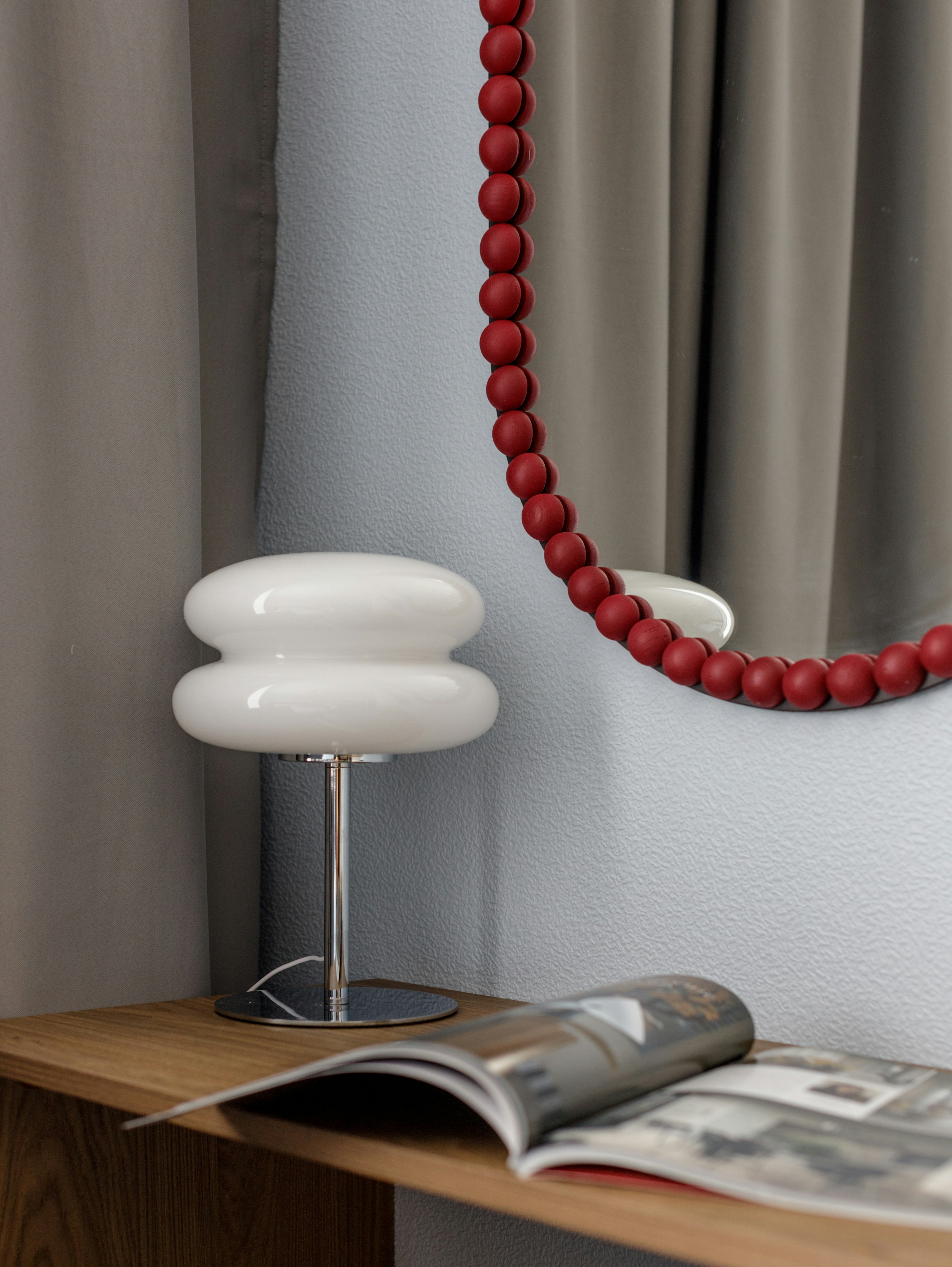 Modern white lamp, open magazine, and red beaded mirror