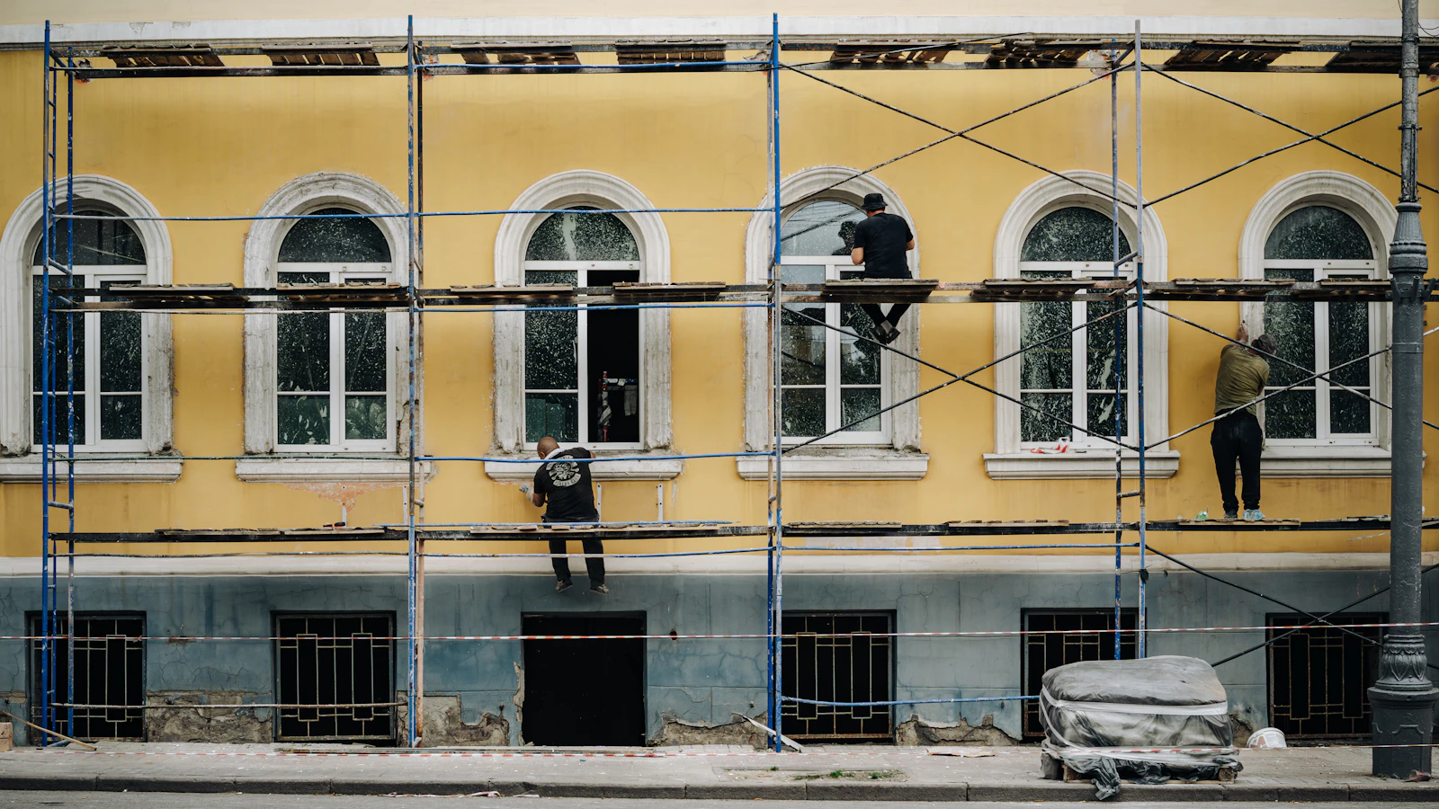 Handwerker auf einem Gerüst vor einer hellen Altbaufassade mit Rundbogenfenstern