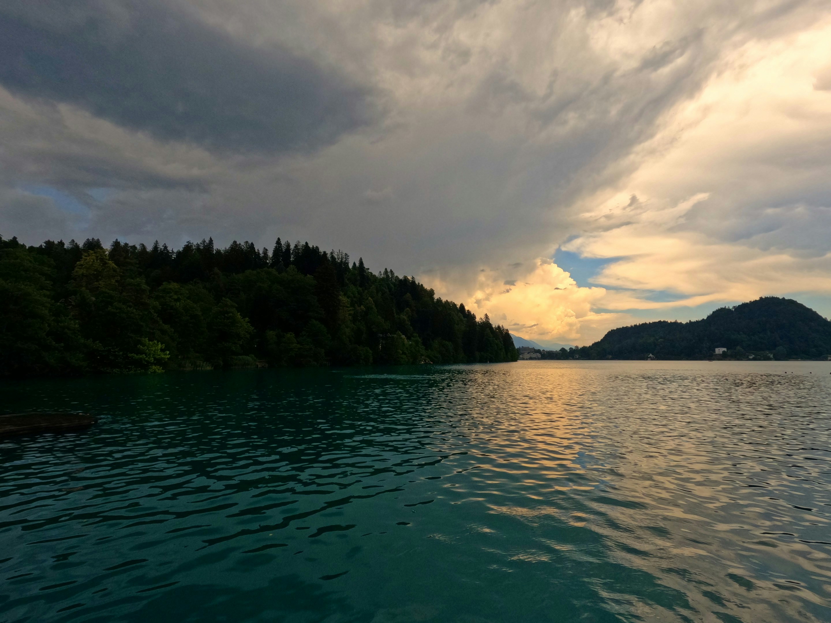 Turquoise lake with forested shore under dramatic cloudy sky