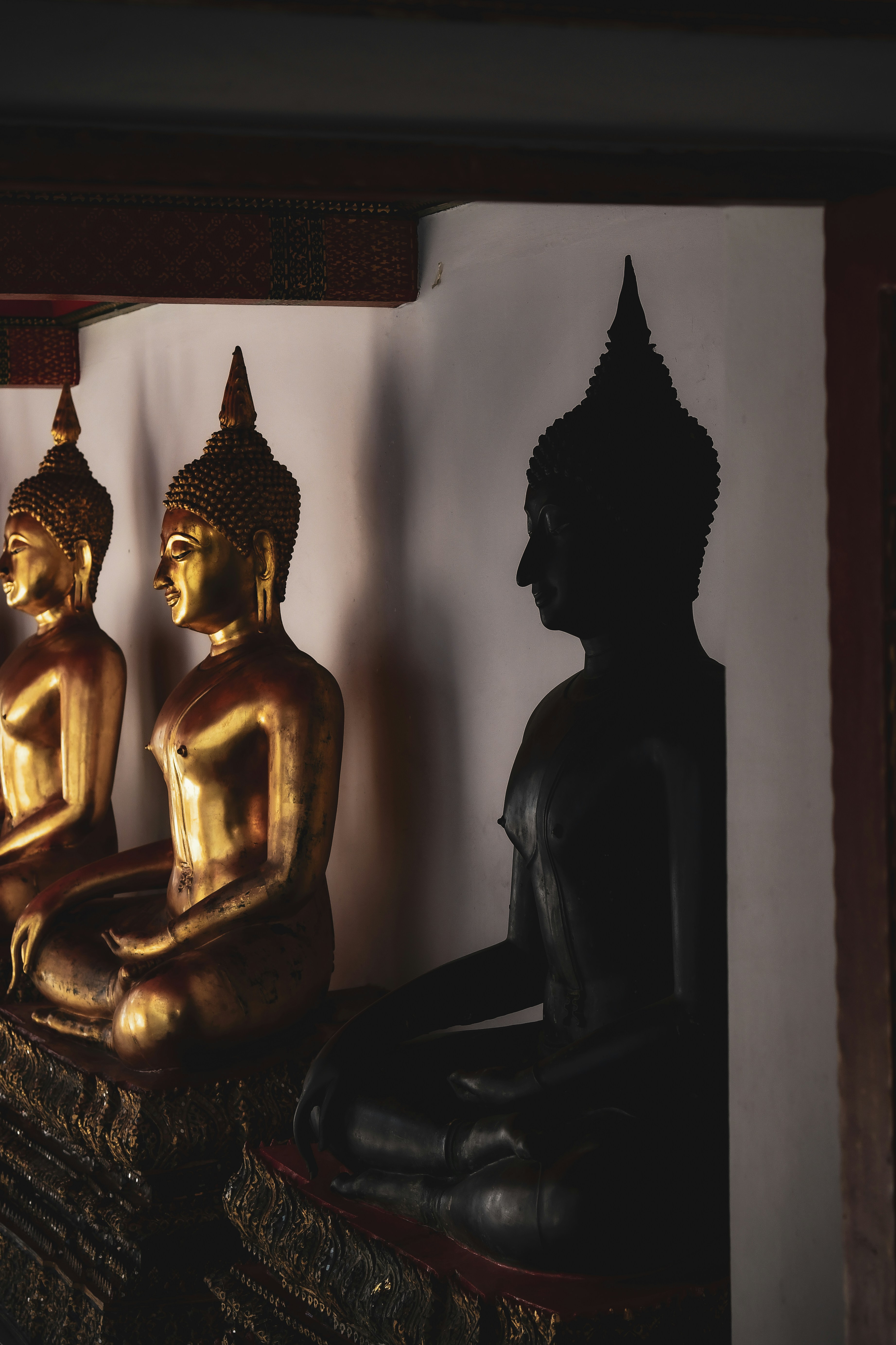 Golden and silhouetted buddha statues in a temple.