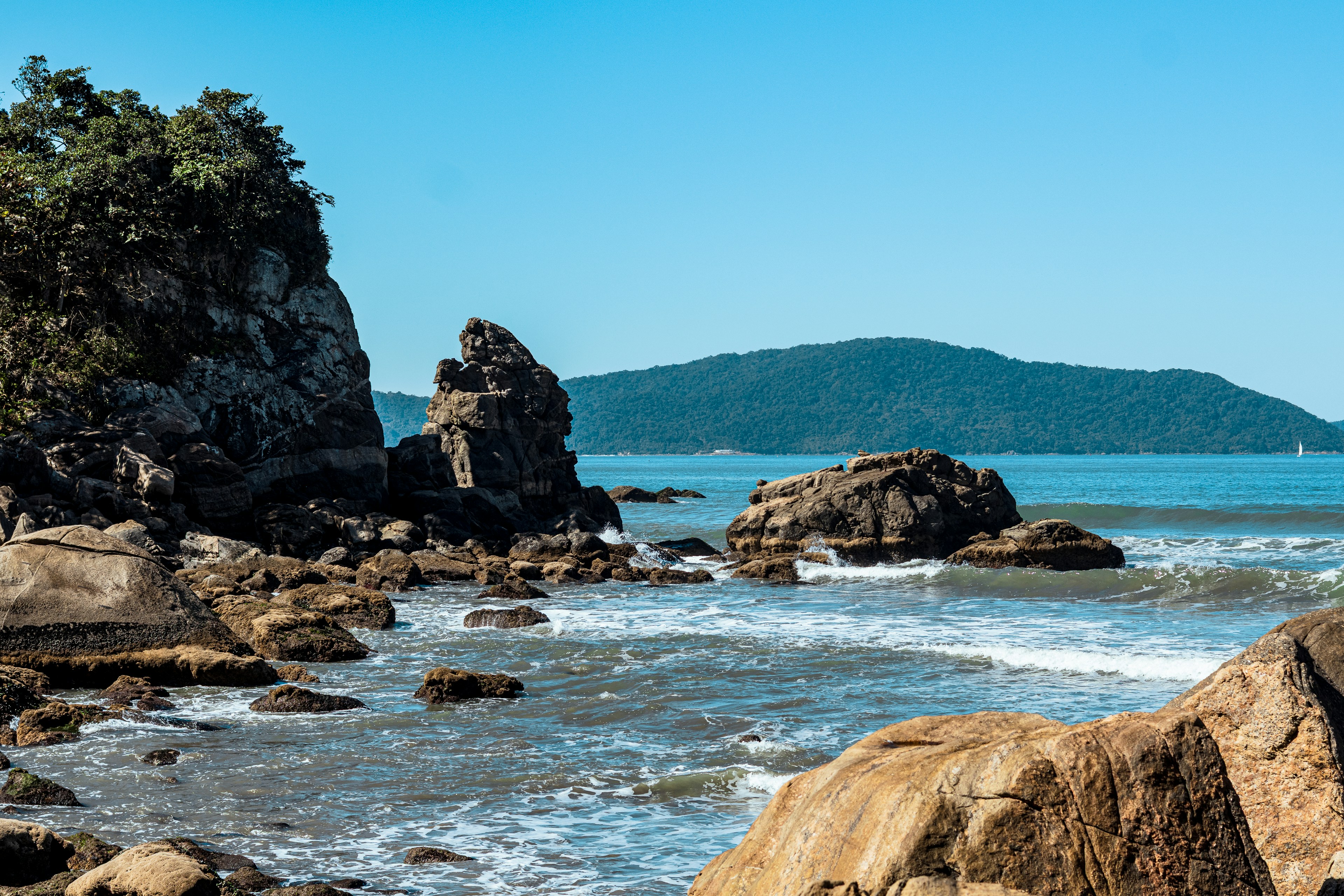 Rocky beach with ocean waves and distant green mountains.