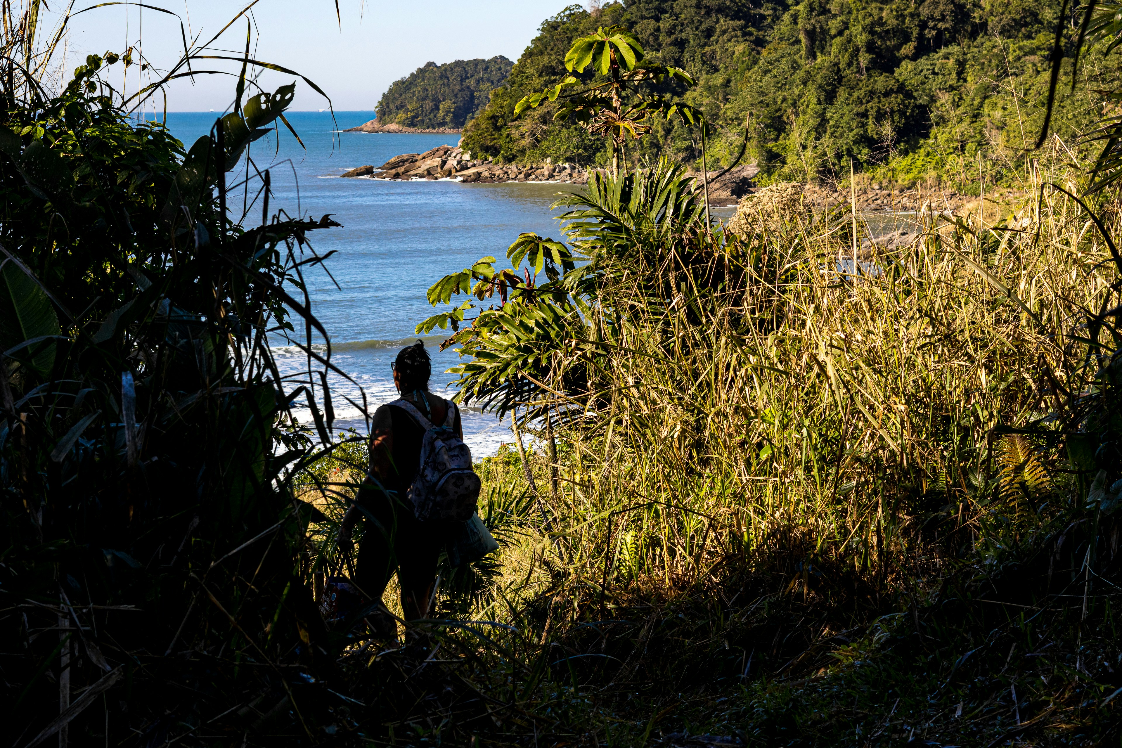 Backpacker walks on a path towards a beautiful, secluded beach.