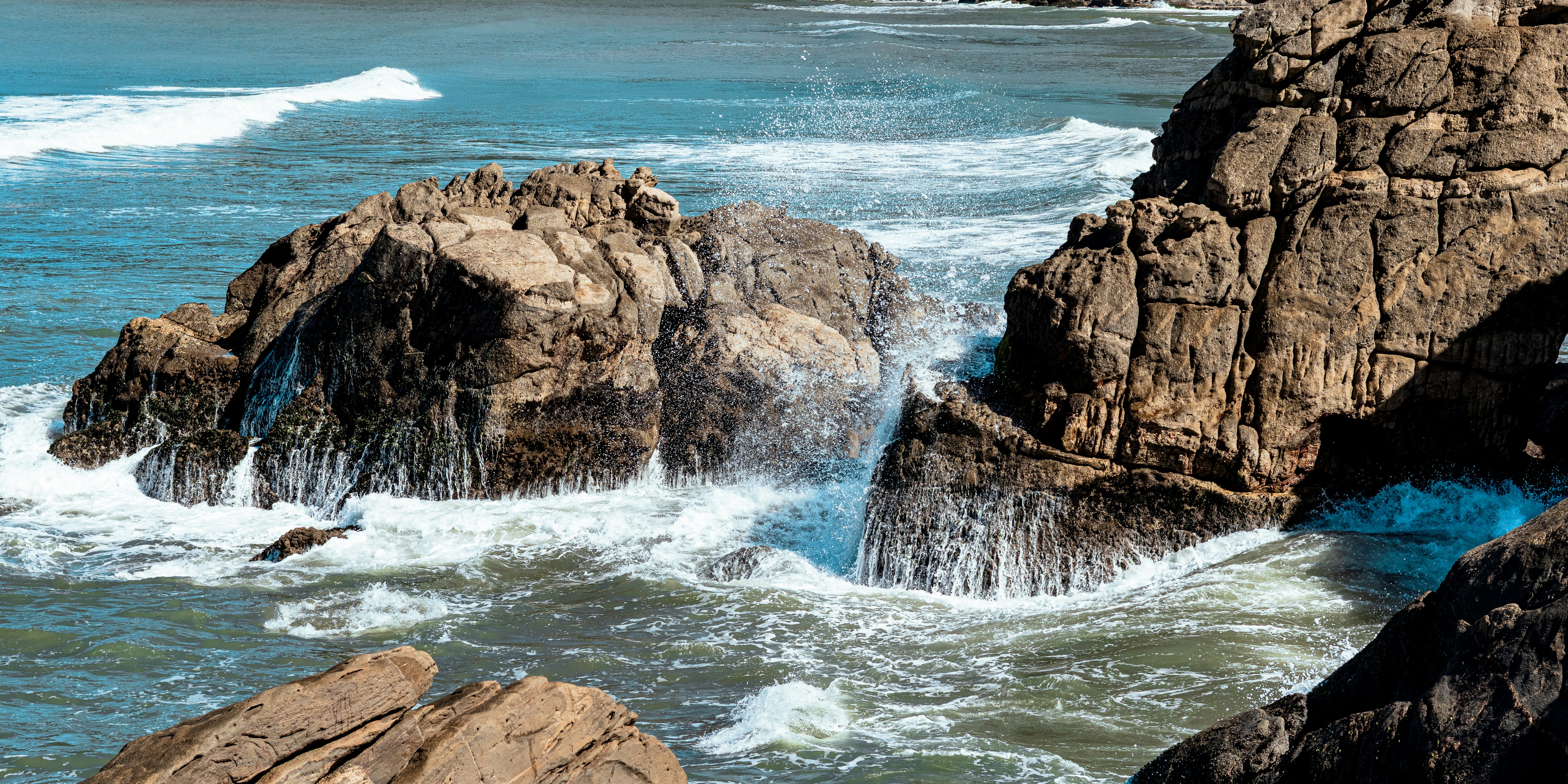 Waves crash against rugged rocks in the blue ocean.