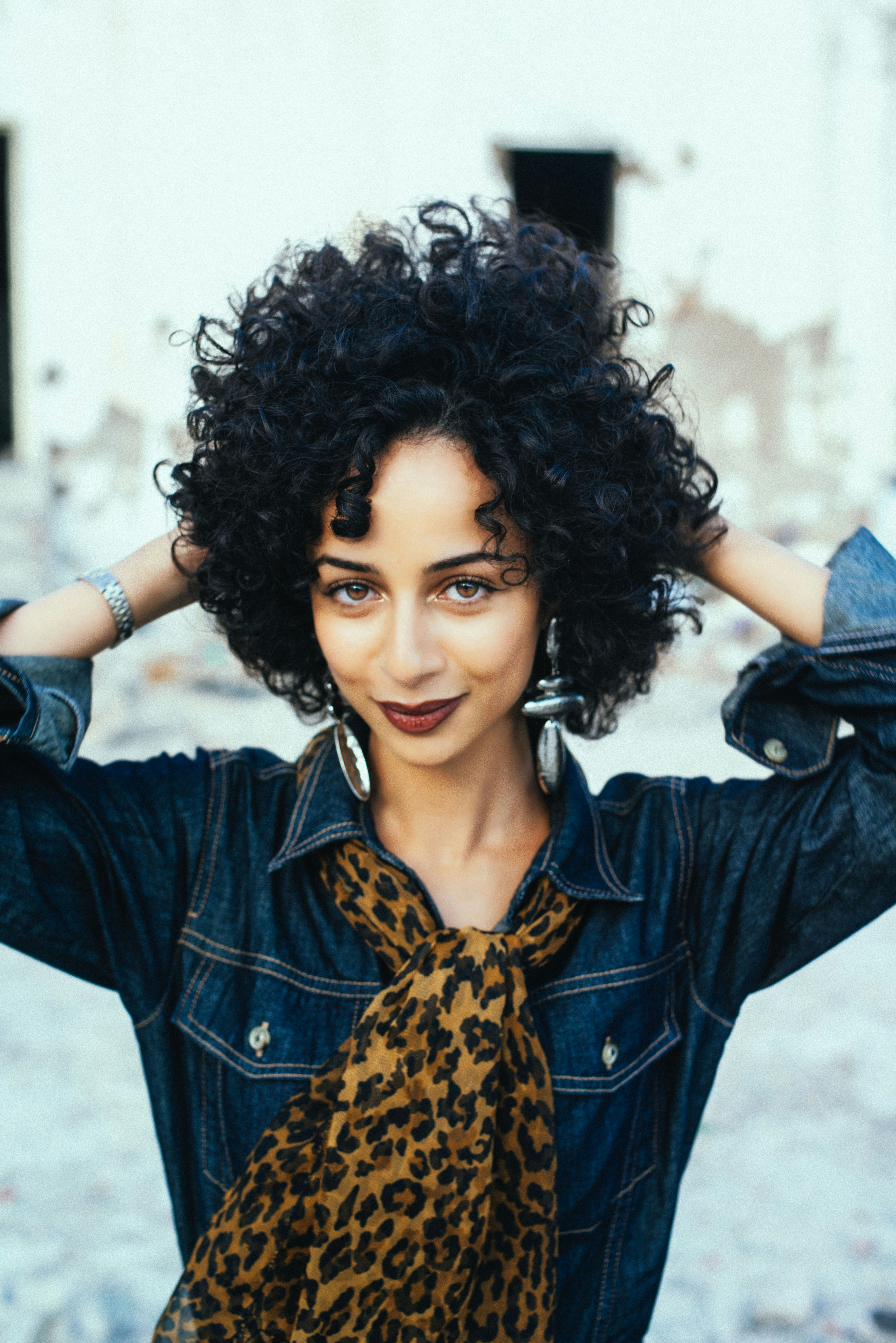 Woman with curly hair, denim jacket, and leopard scarf