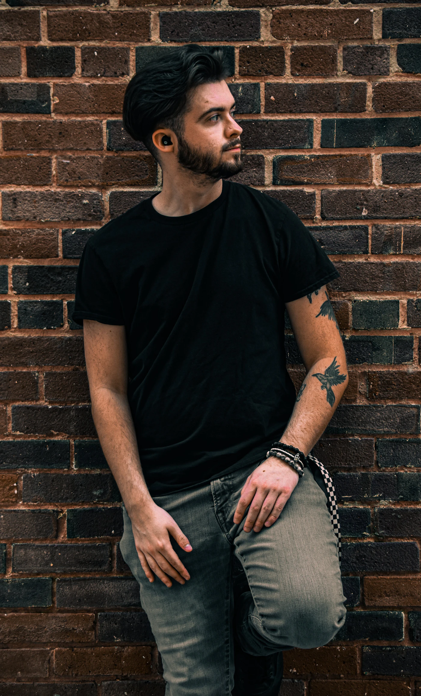 Man in a black t-shirt leaning on a brick wall