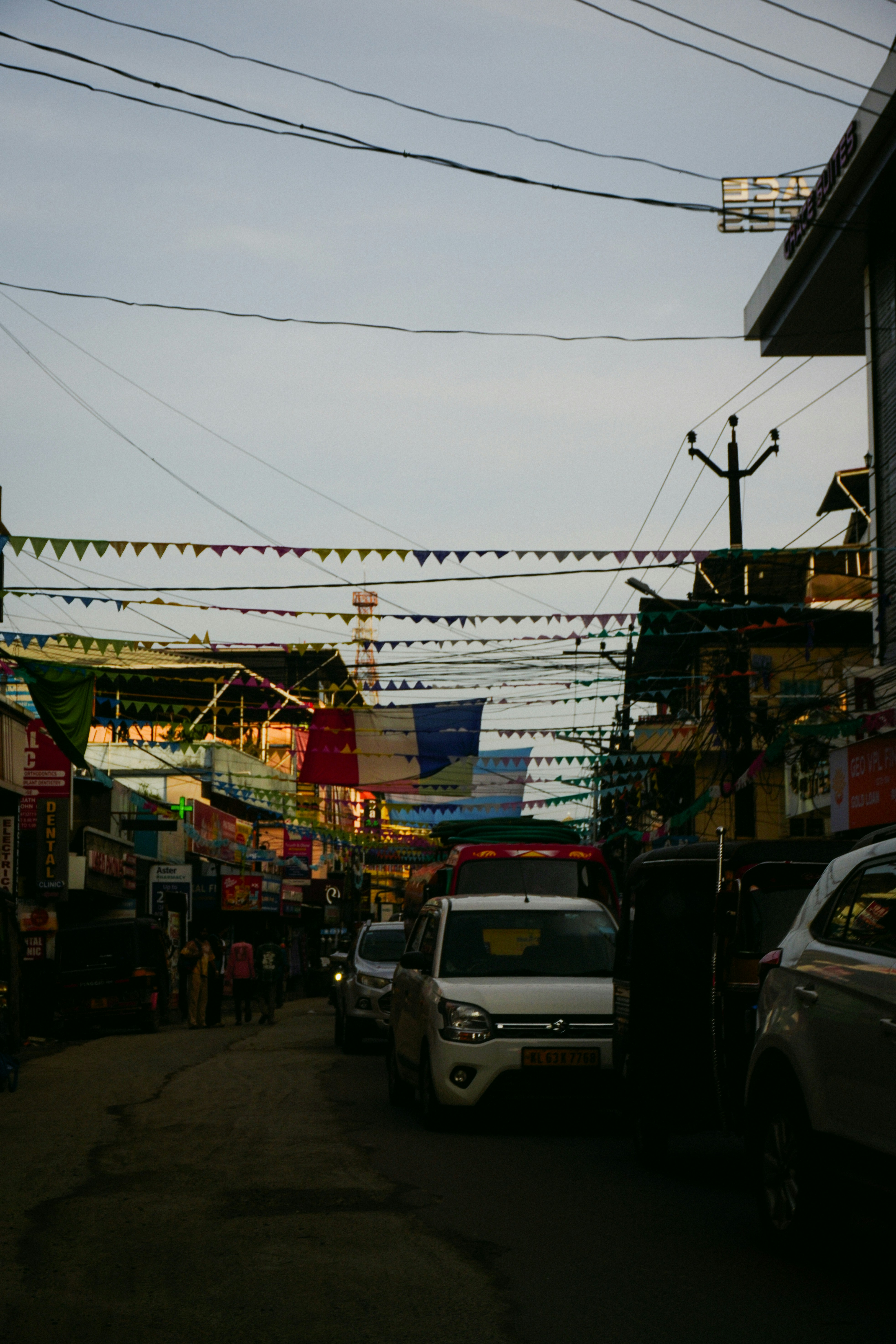 Urban street scene with overhead wires, colorful banners, and vehicles.