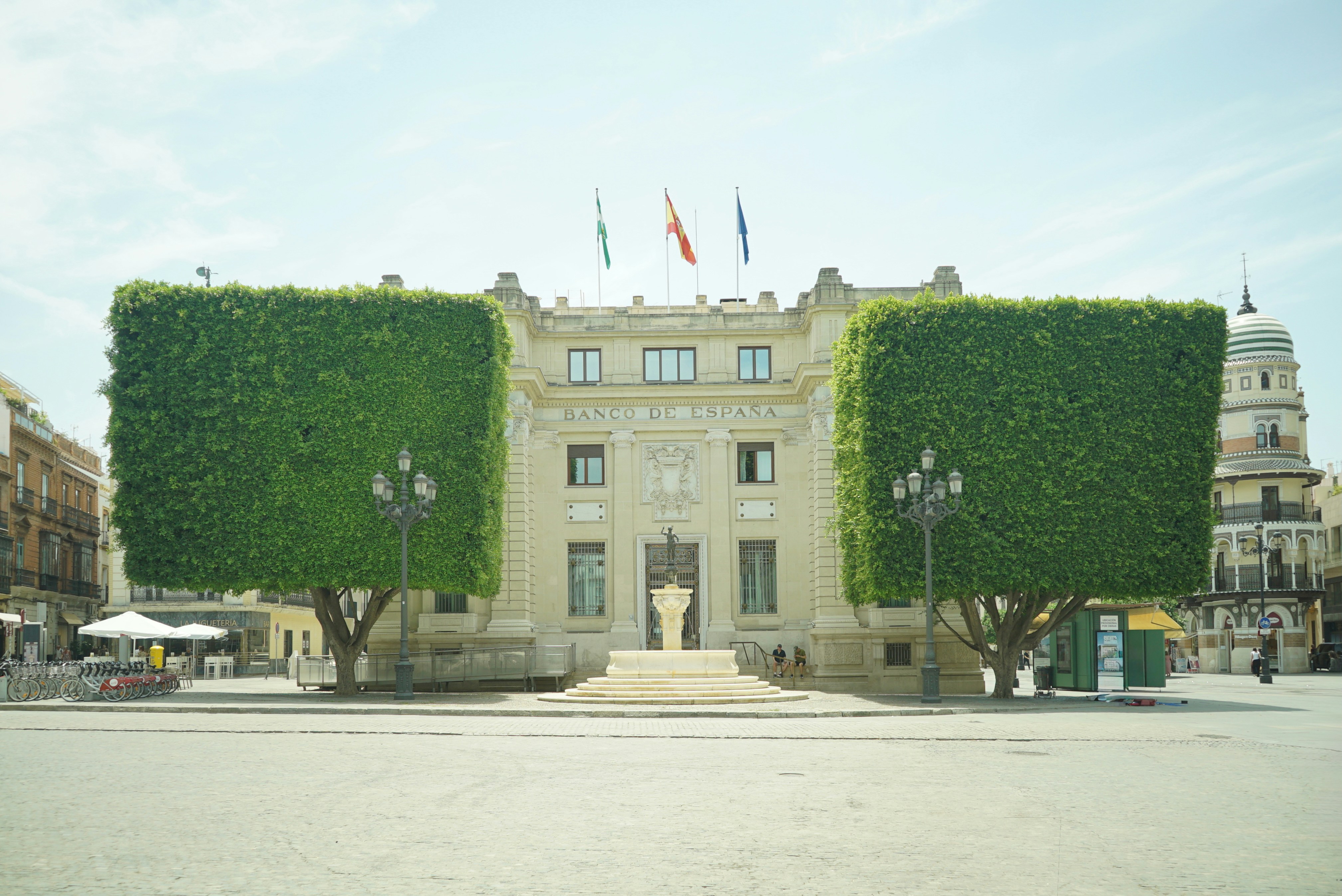 Grand building flanked by two square-shaped trees in a plaza.