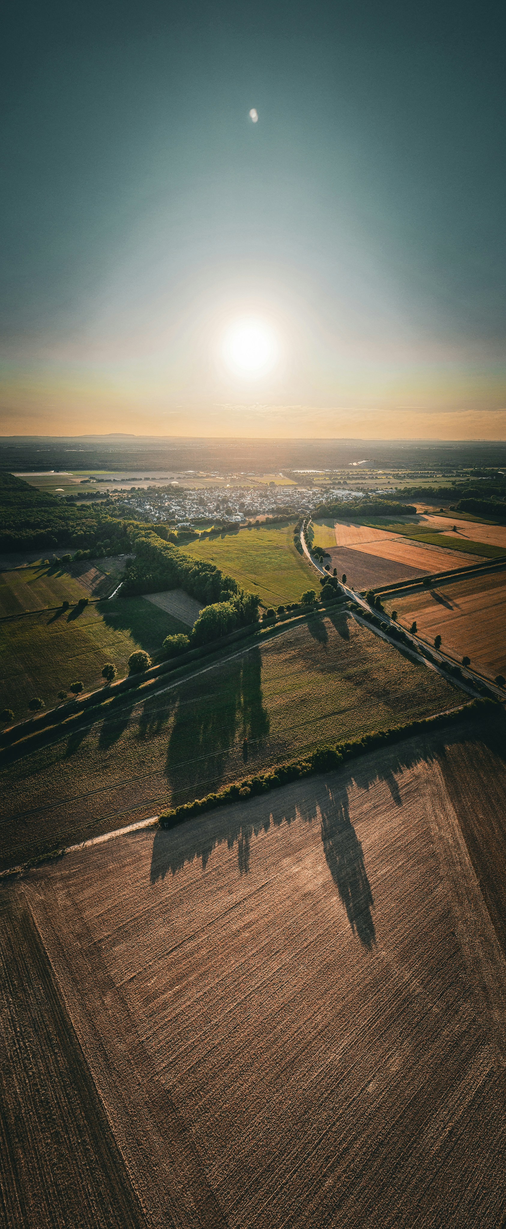 Golden hour aerial view of fields, trees, and distant town.