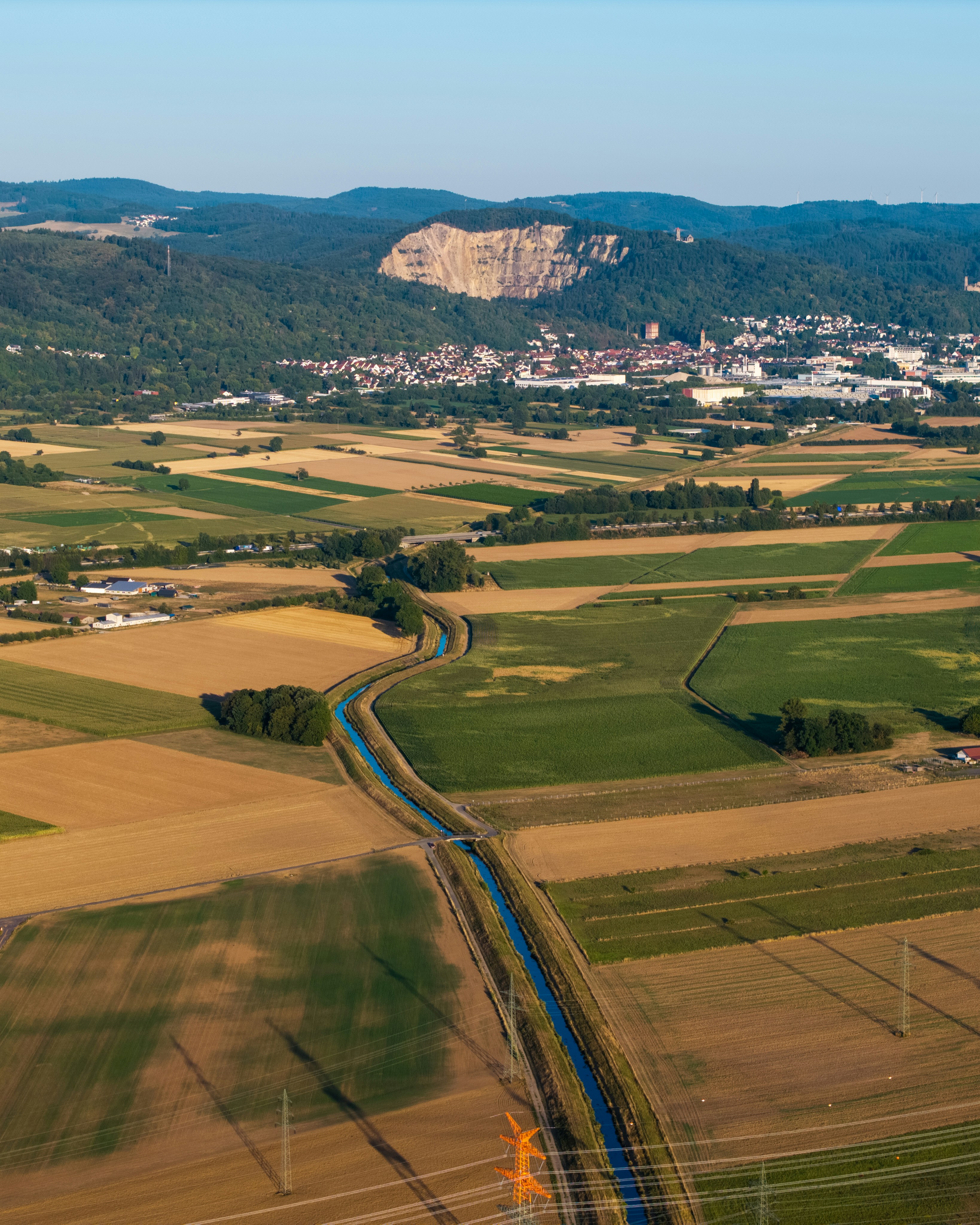 Agricultural fields, winding canal, distant town, and prominent cliff.