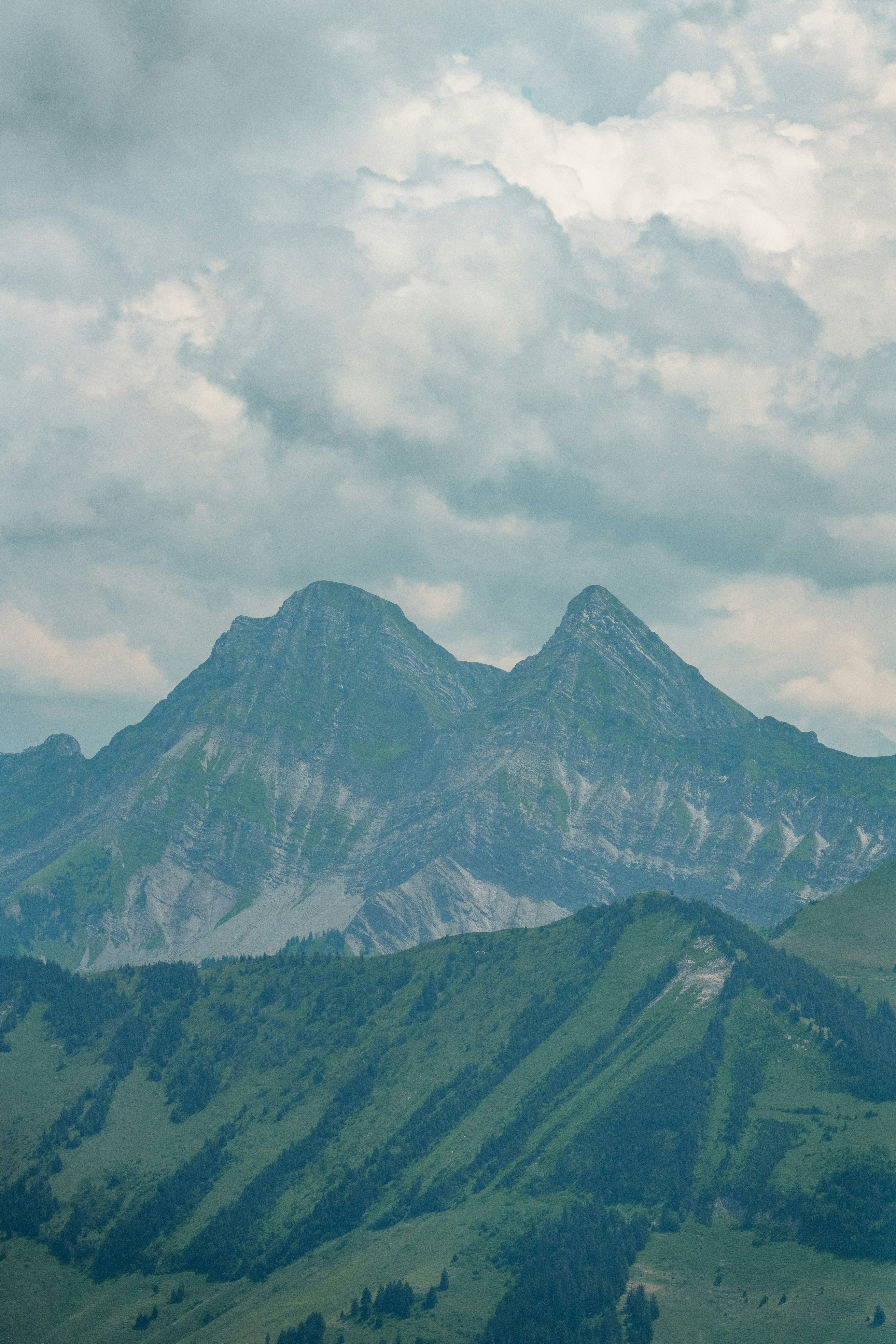 Puncak gunung yang megah di bawah langit berawan dengan bukit-bukit hijau.