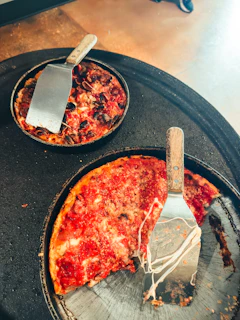 Two deep-dish pizzas with spatulas, one with a slice removed