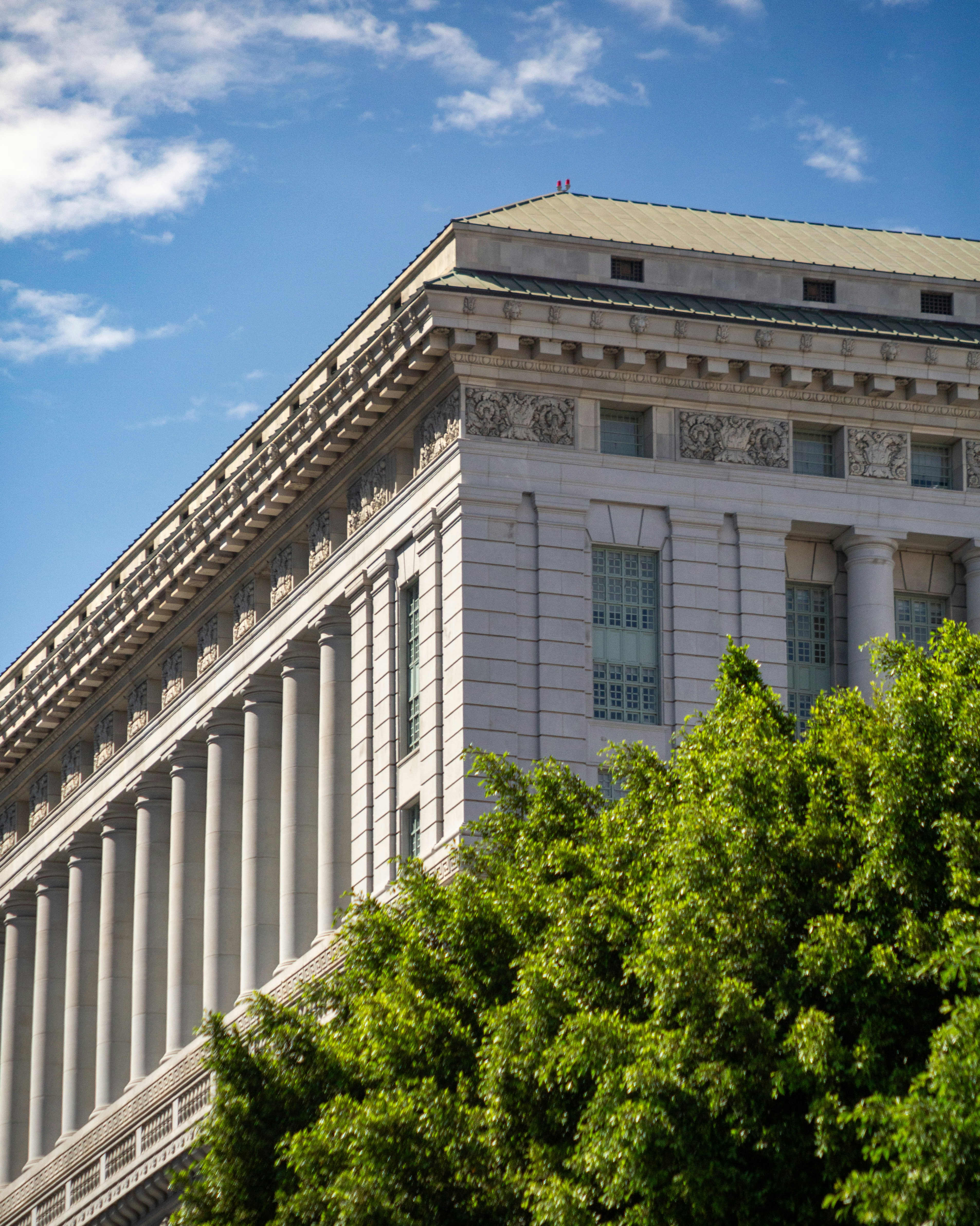 Classical building with columns, green trees, and blue sky.