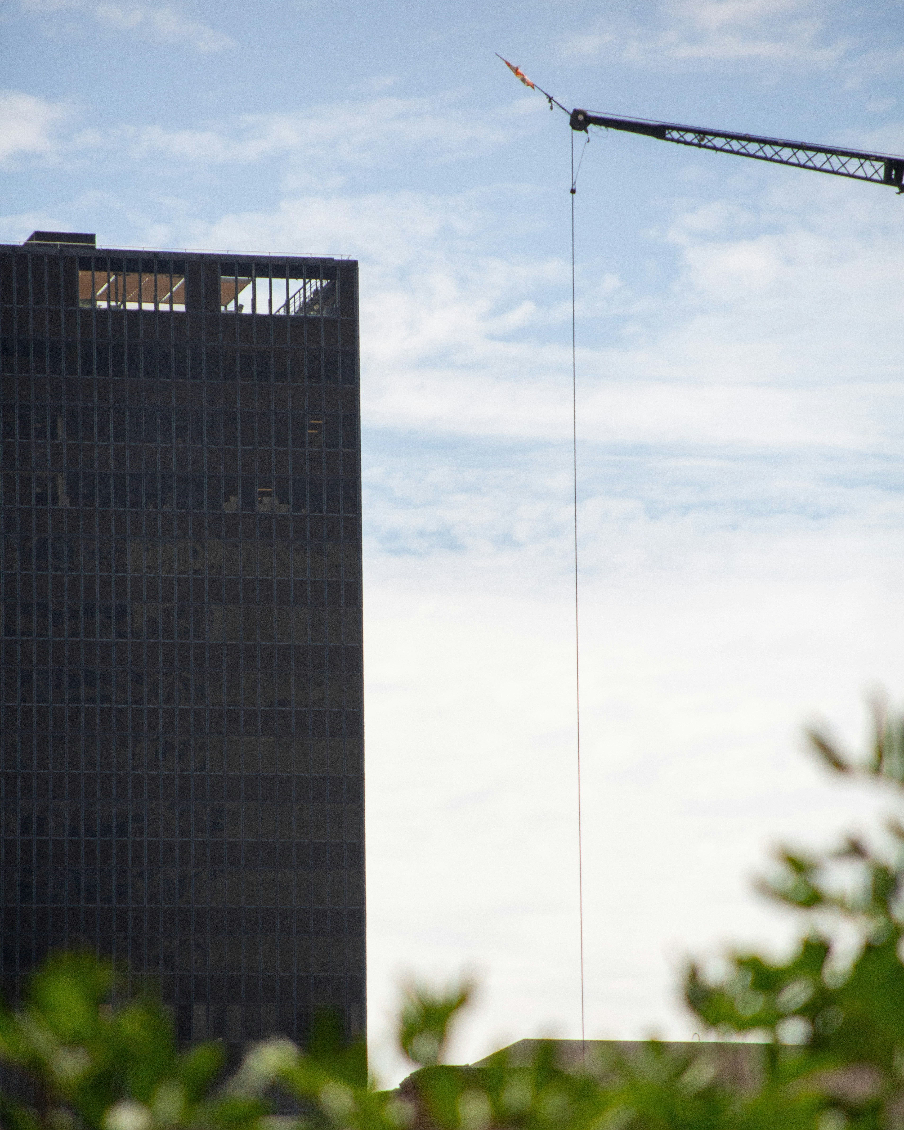 Tall dark building and construction crane against cloudy sky.