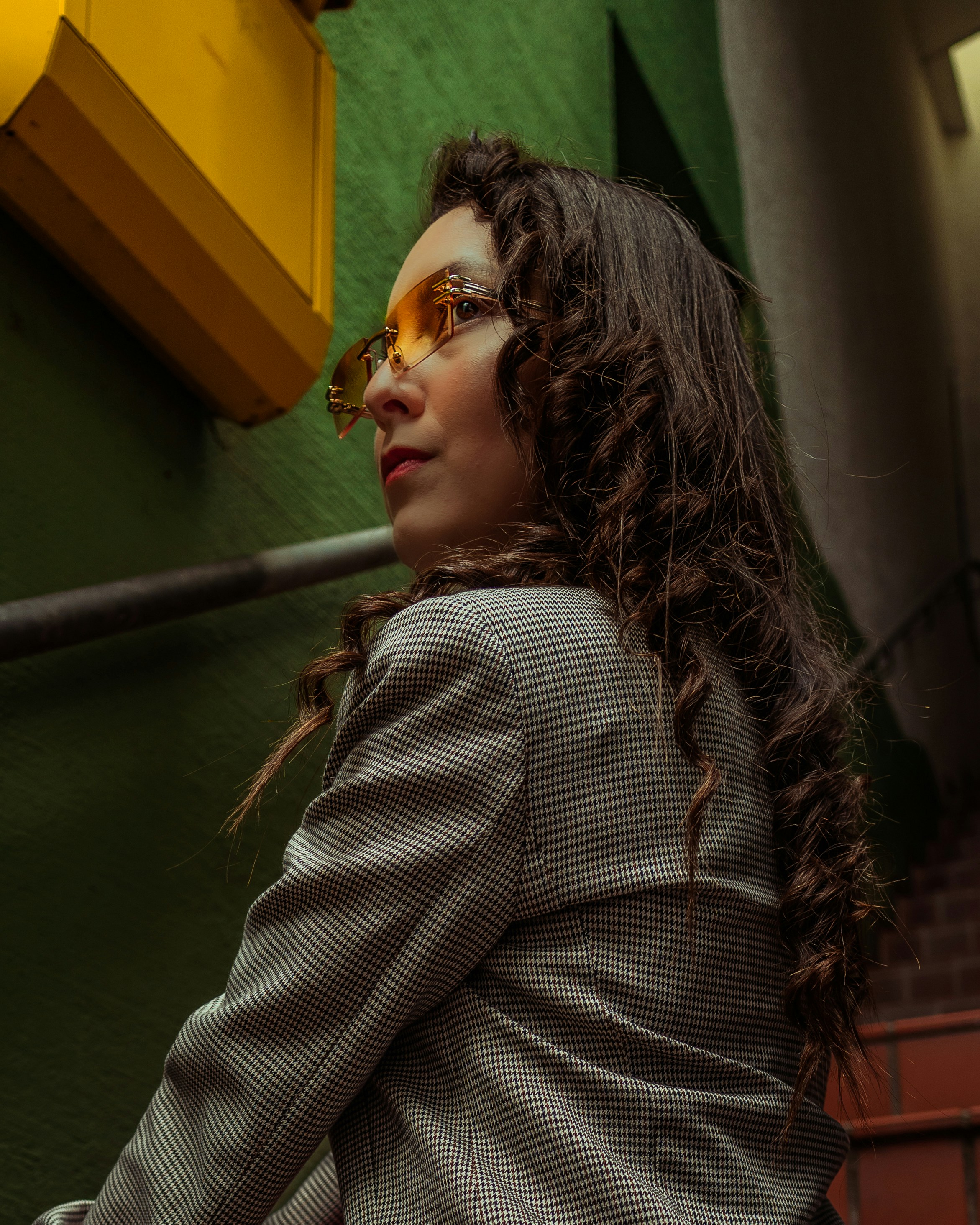 Lockige Frau mit Sonnenbrille an einer grünen Wand.