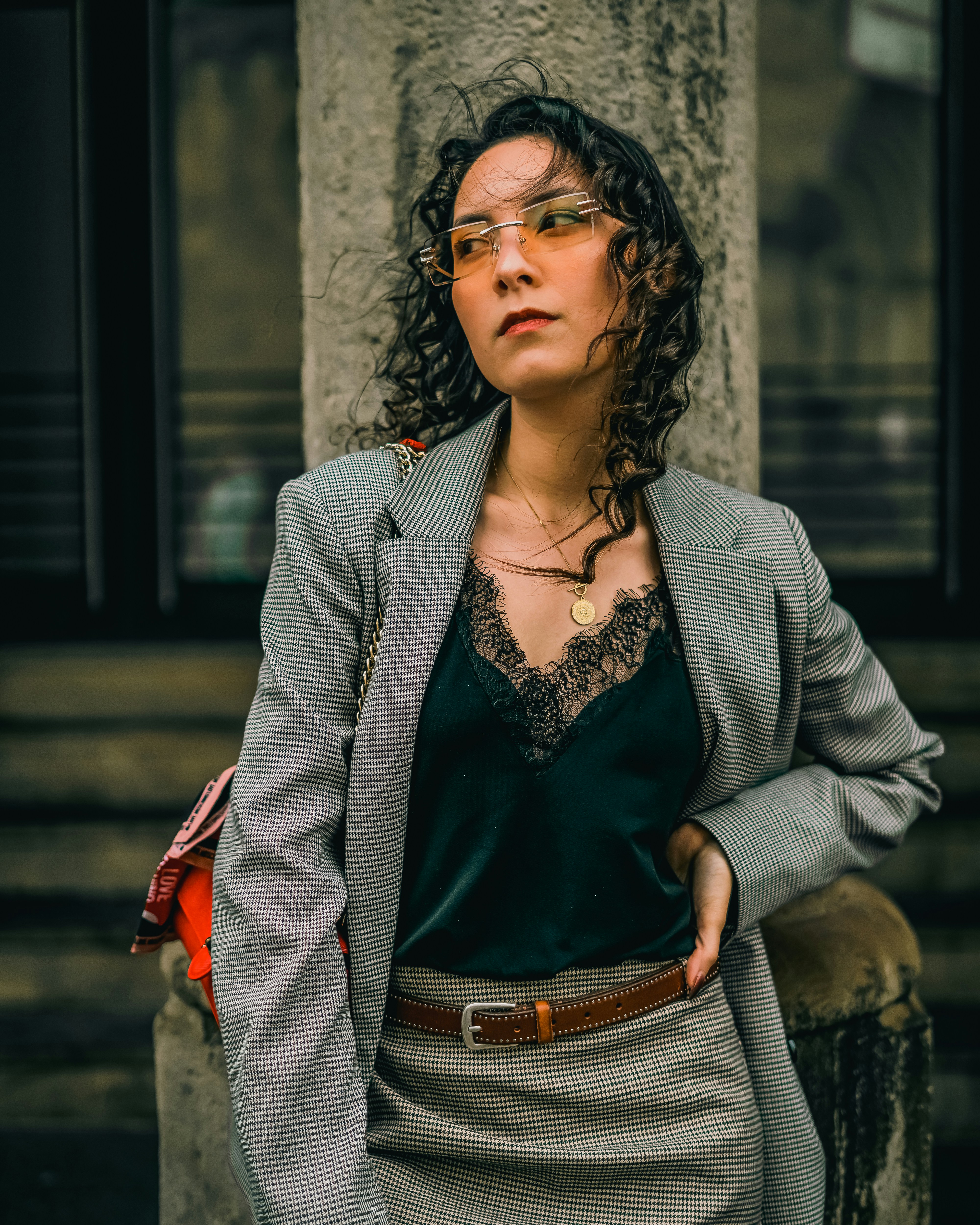 Frau mit lockigem Haar und Sonnenbrille lehnt sich an eine Säule.