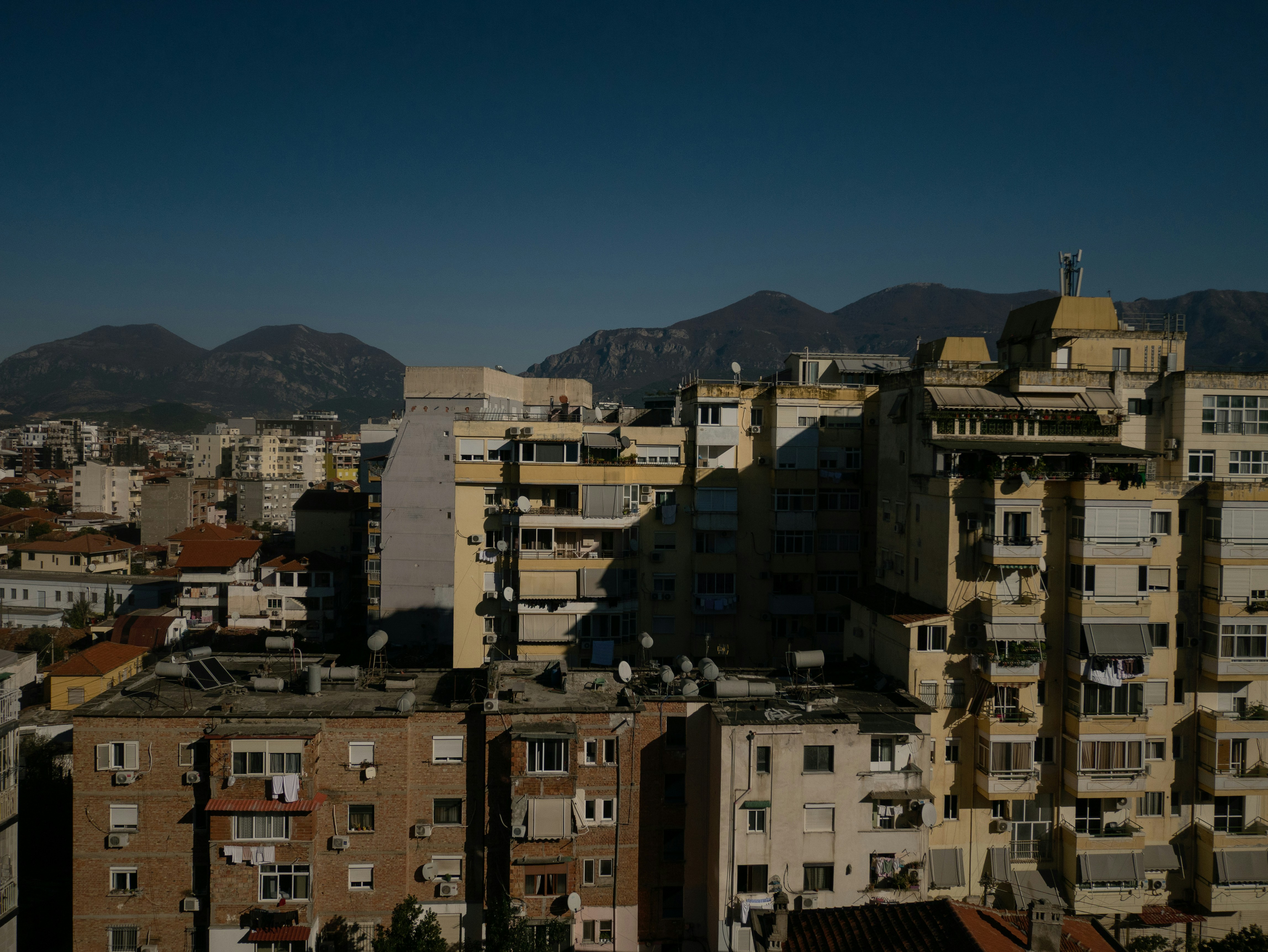Dense cityscape with residential buildings and mountains under blue sky