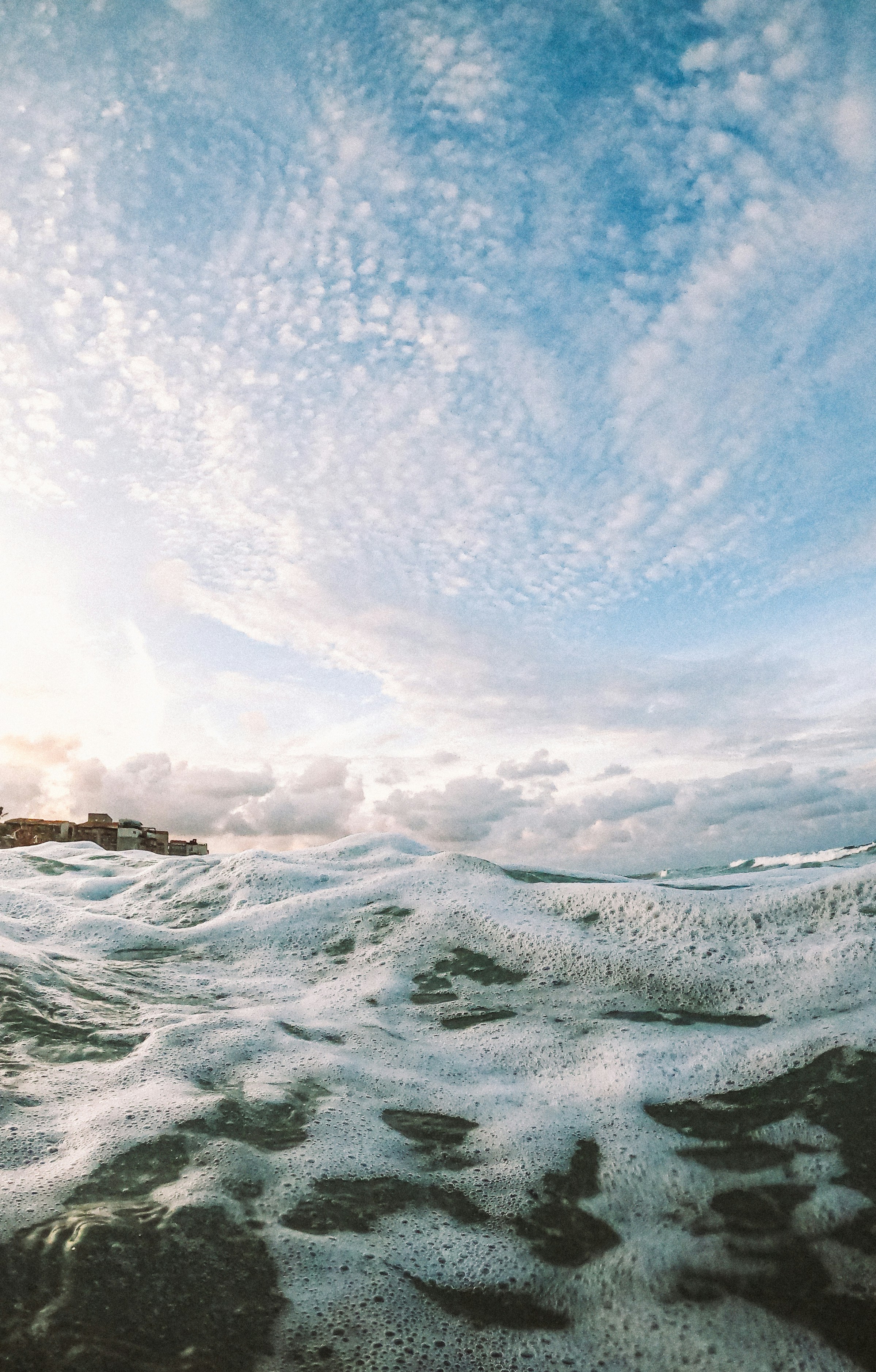 Foamy ocean waves under a cloudy sky with distant land.