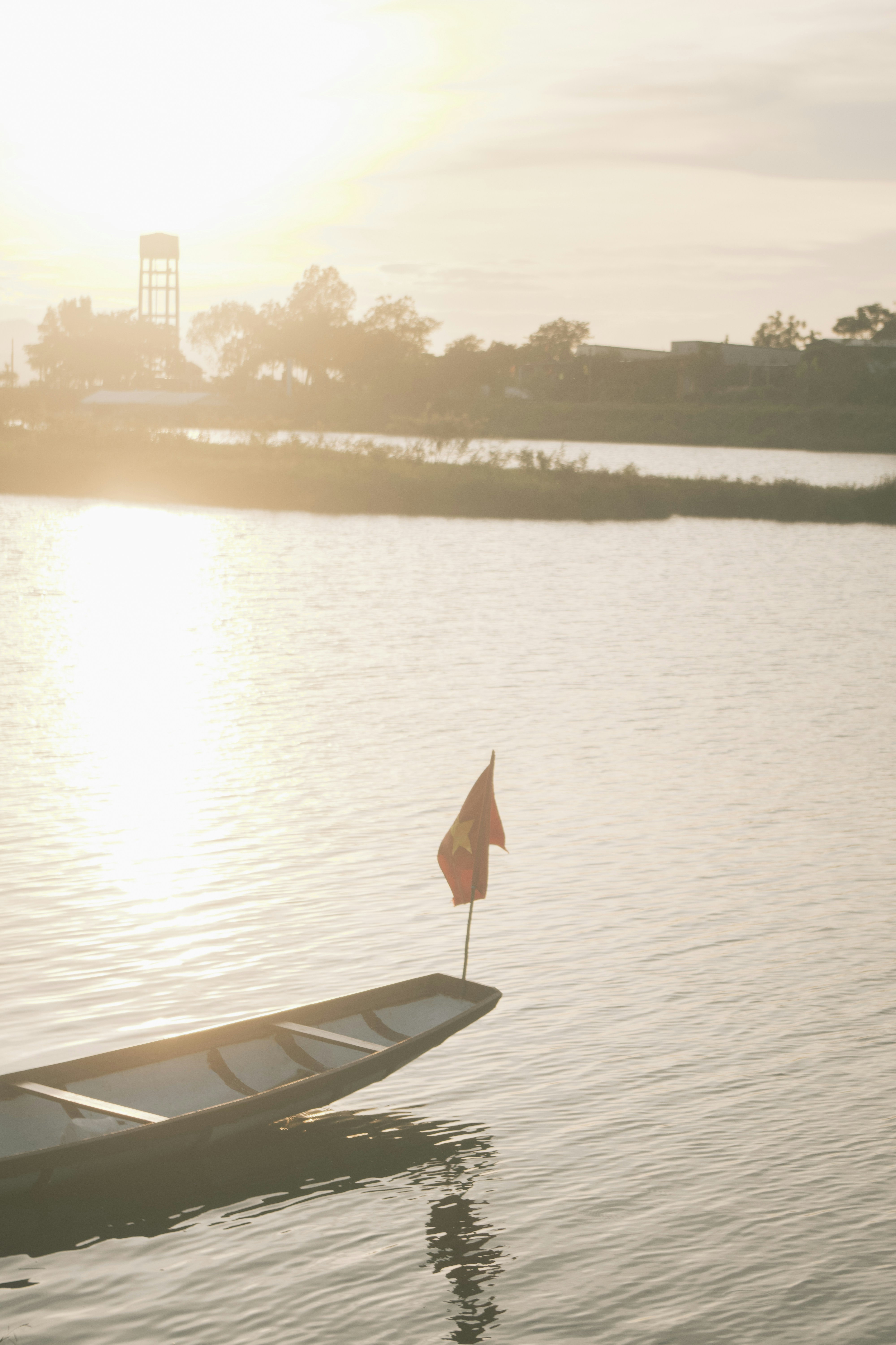 A boat with a flag on a river at sunrise.