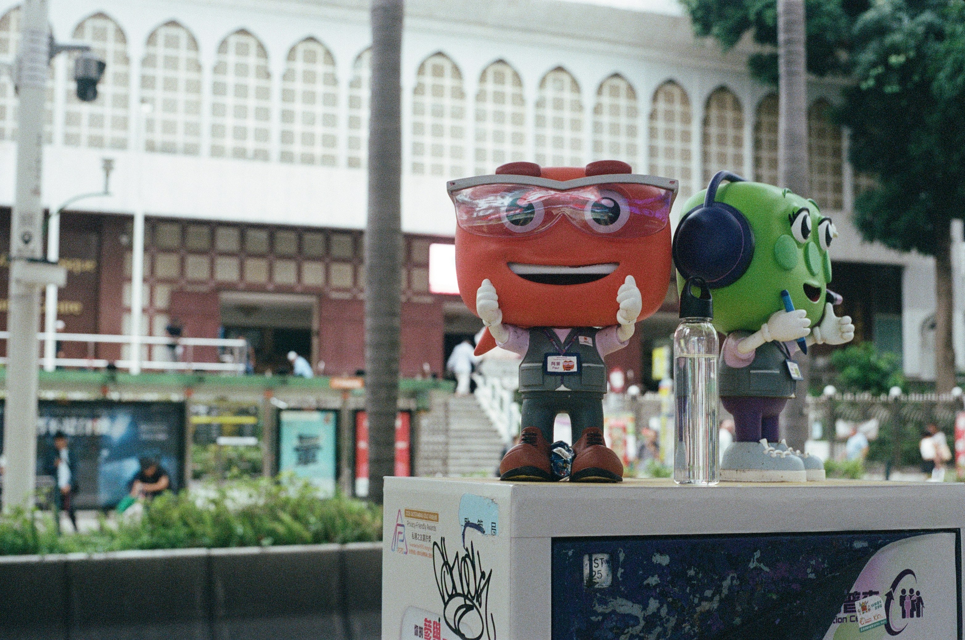 Mascotes de desenho vermelho e verde em um suporte ao ar livre.