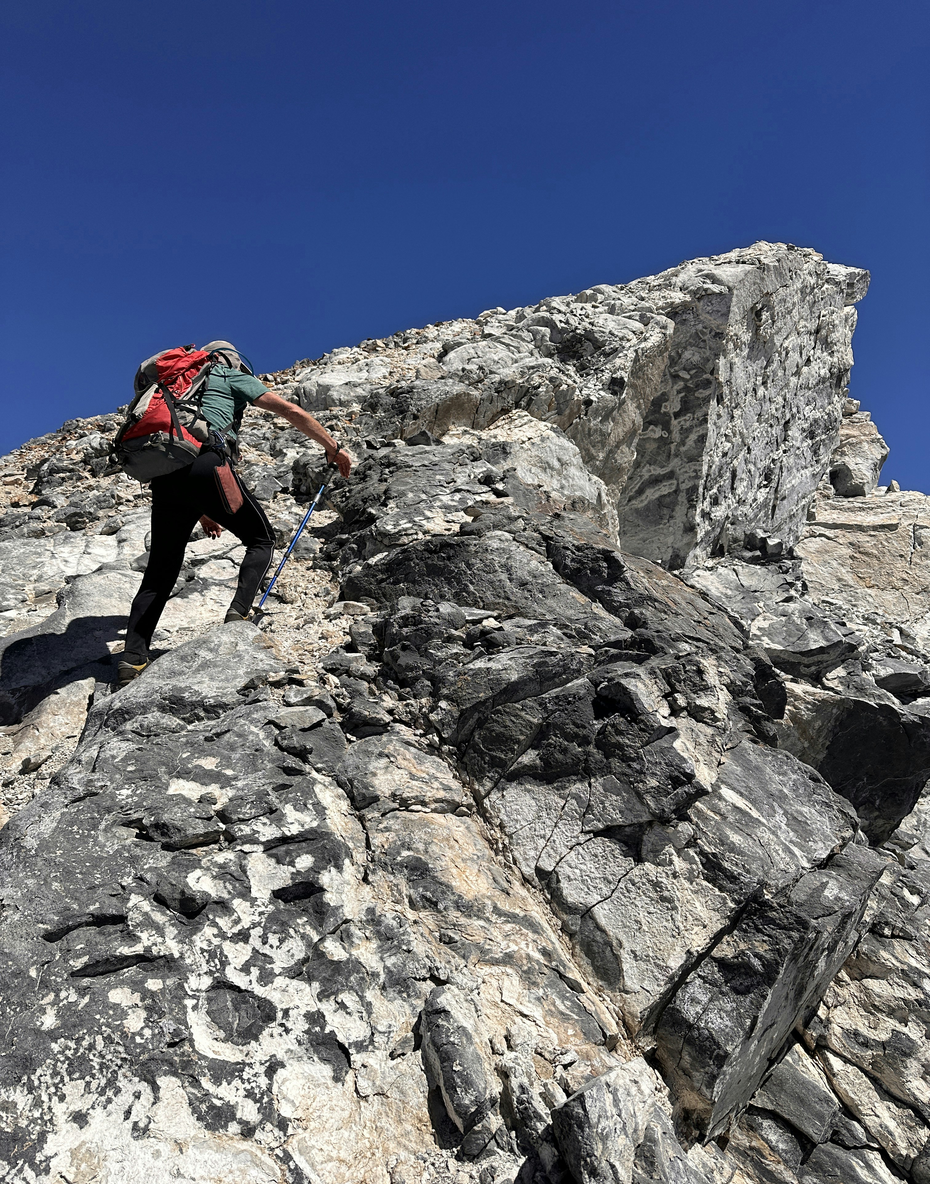 Hiker ascending a rugged mountain peak against a blue sky.