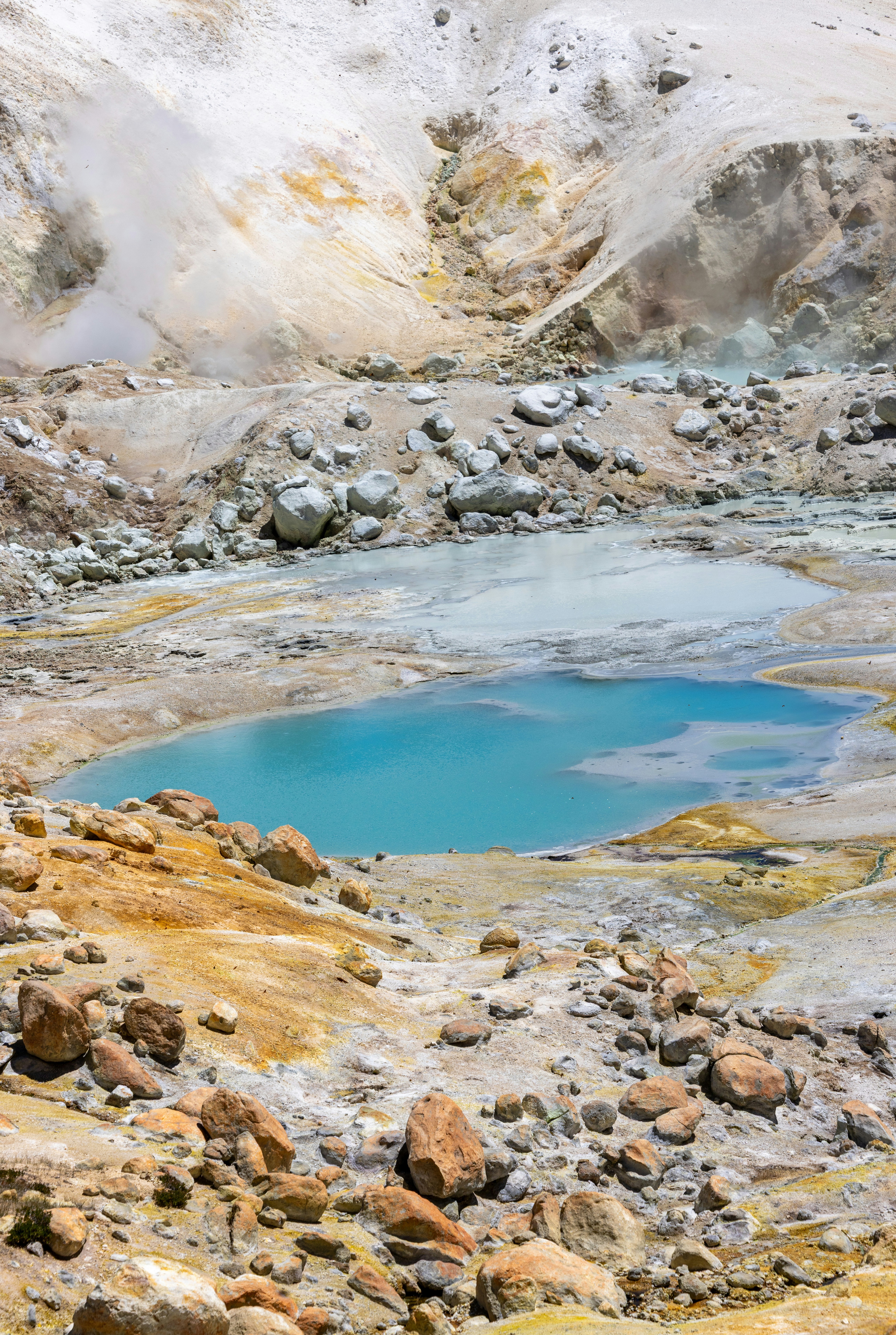 A vibrant blue geothermal pool in a rocky, steaming landscape.
