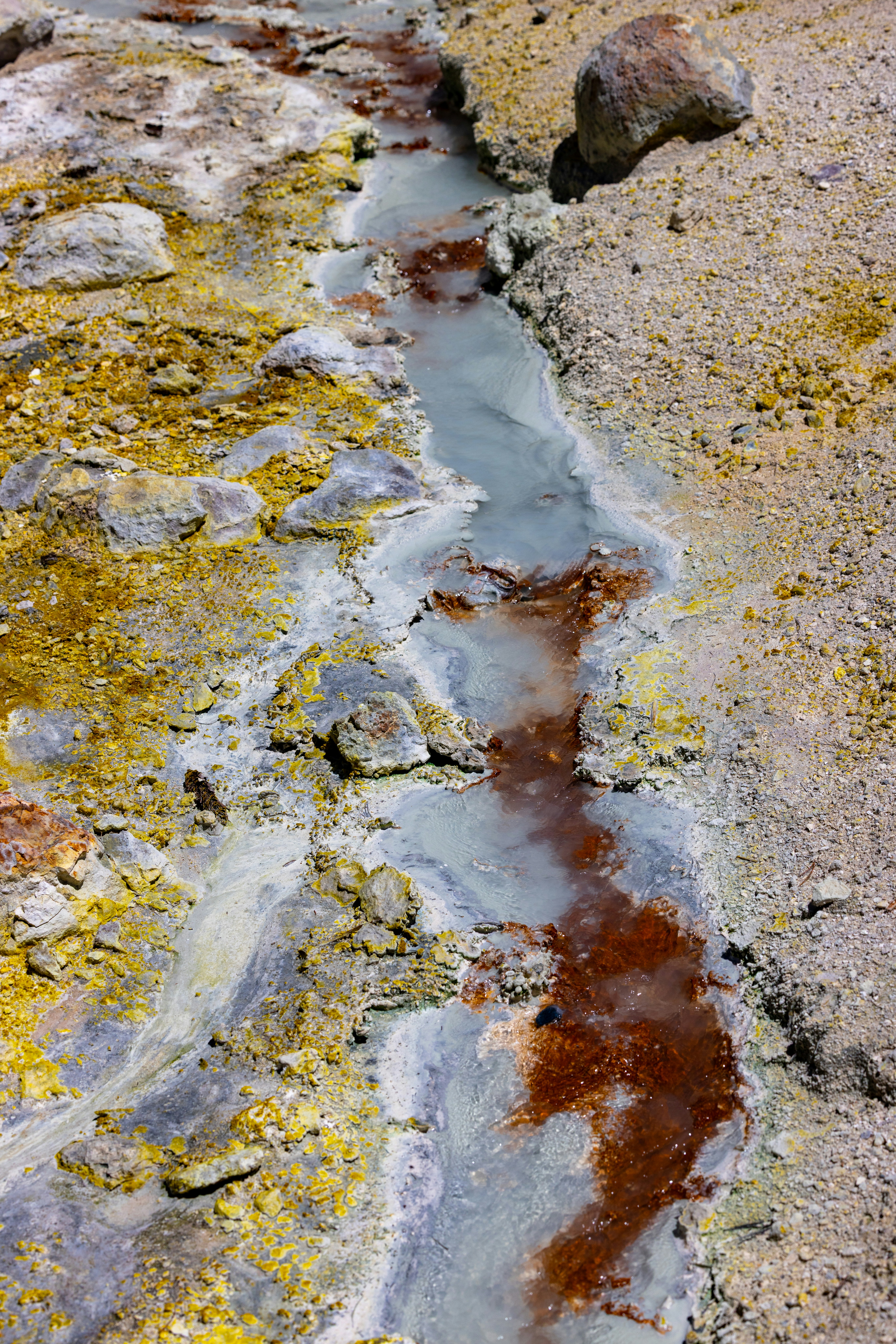A stream of mineral-rich water flows through colorful volcanic terrain.