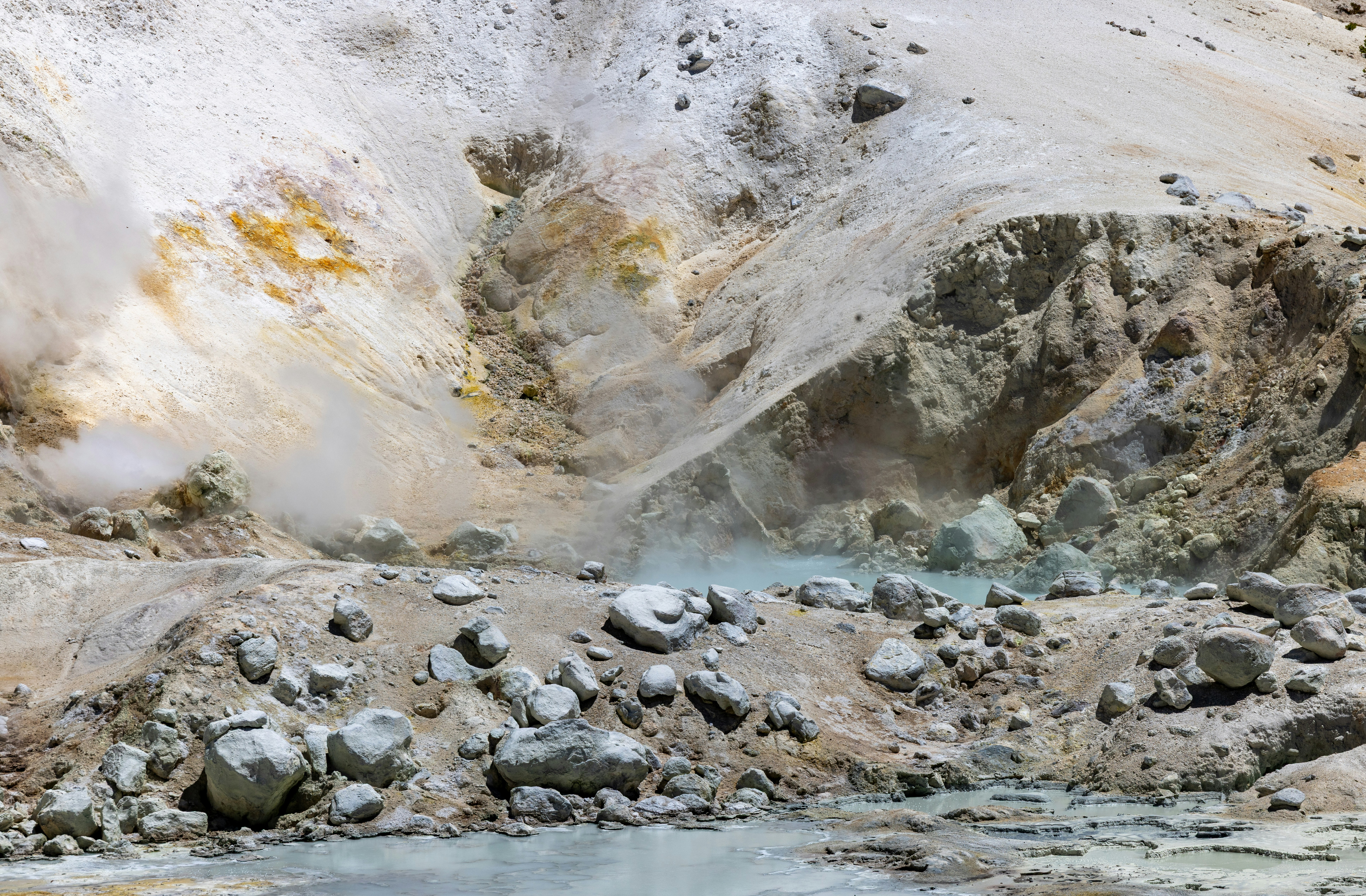 Steaming volcanic landscape with rocky terrain and a geothermal pool.