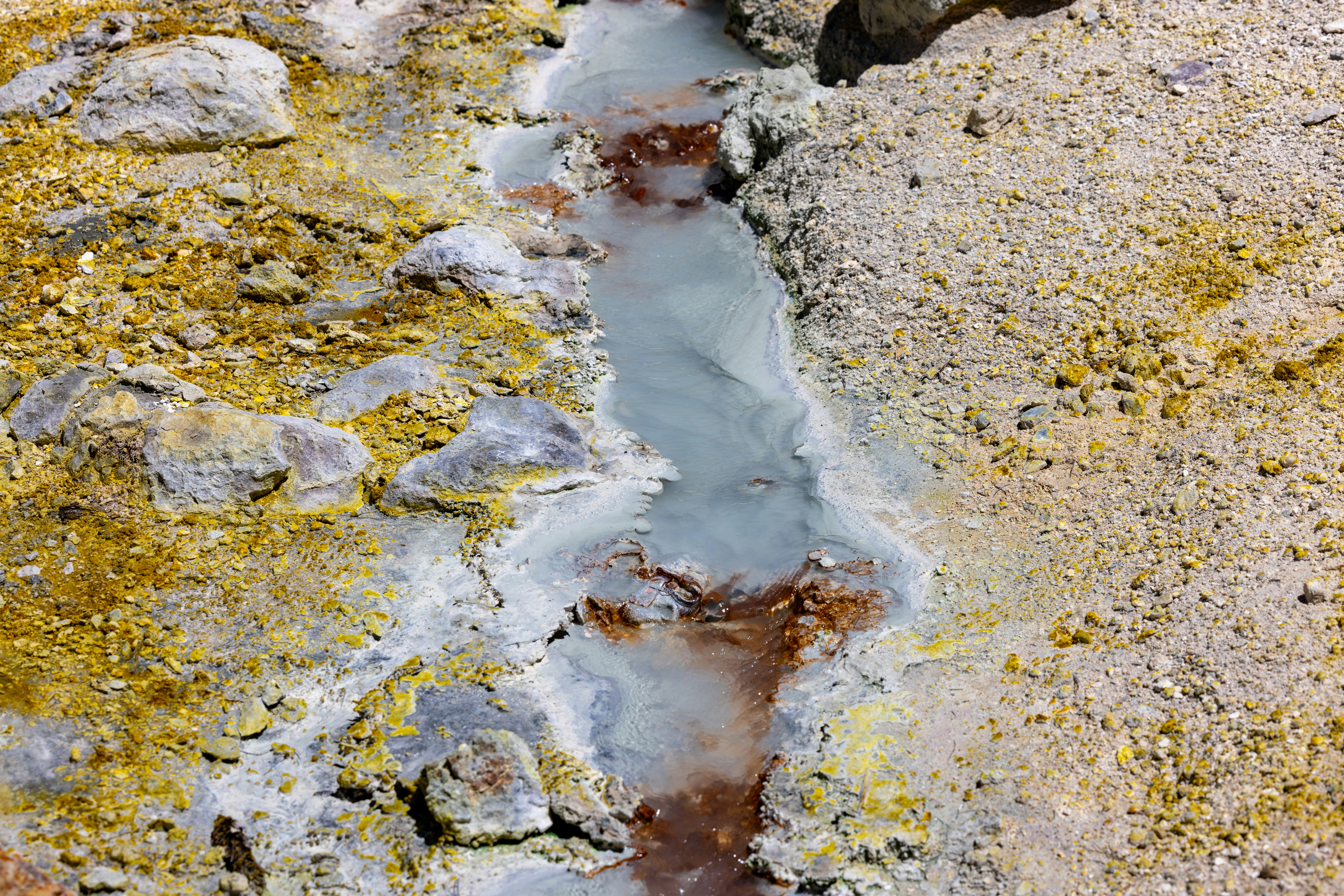 Geothermal stream flows through colorful, mineral-rich volcanic rock.