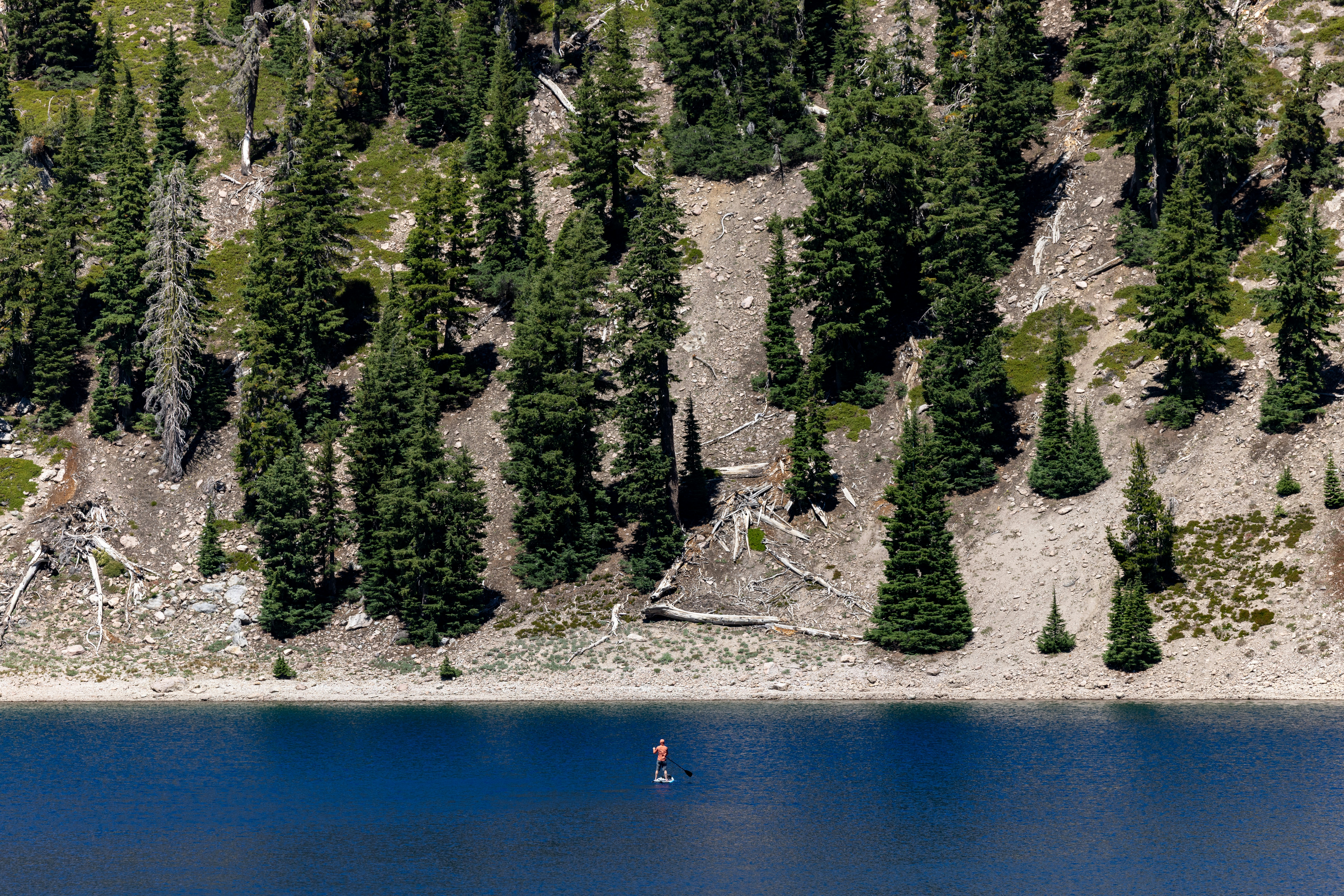 Person paddleboarding on a blue lake with a forested hillside.