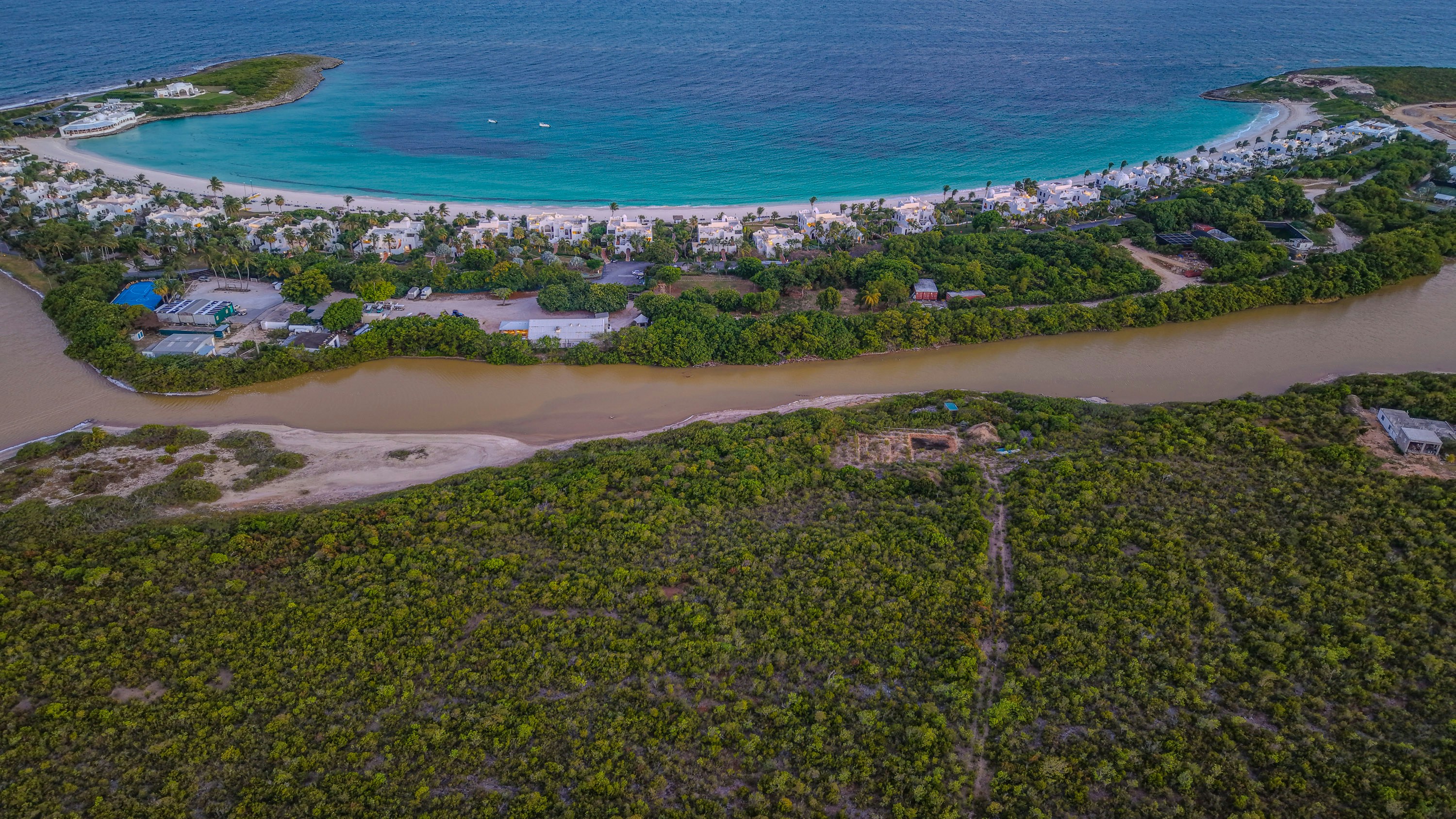 Turquoise bay, sandy beach, river, and lush green landscape.