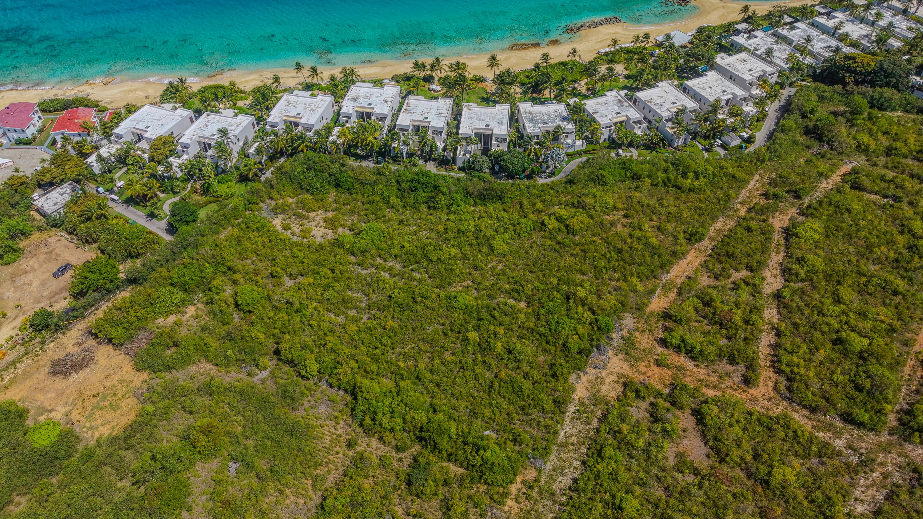 Green land, white coastal buildings, sandy beach, and turquoise ocean