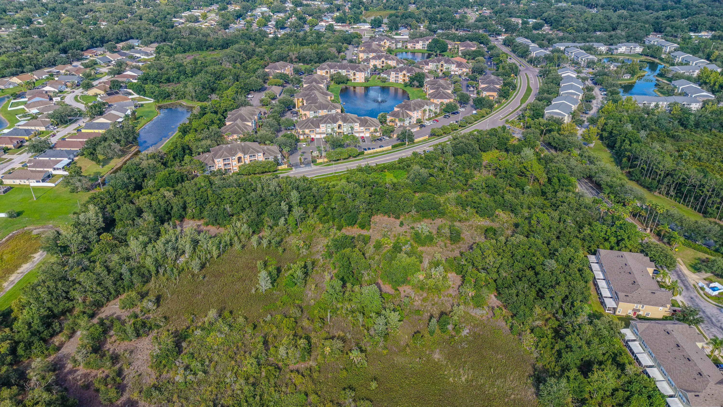 Aerial view of suburban homes and curving streets around ponds beside a large tract of undeveloped land.