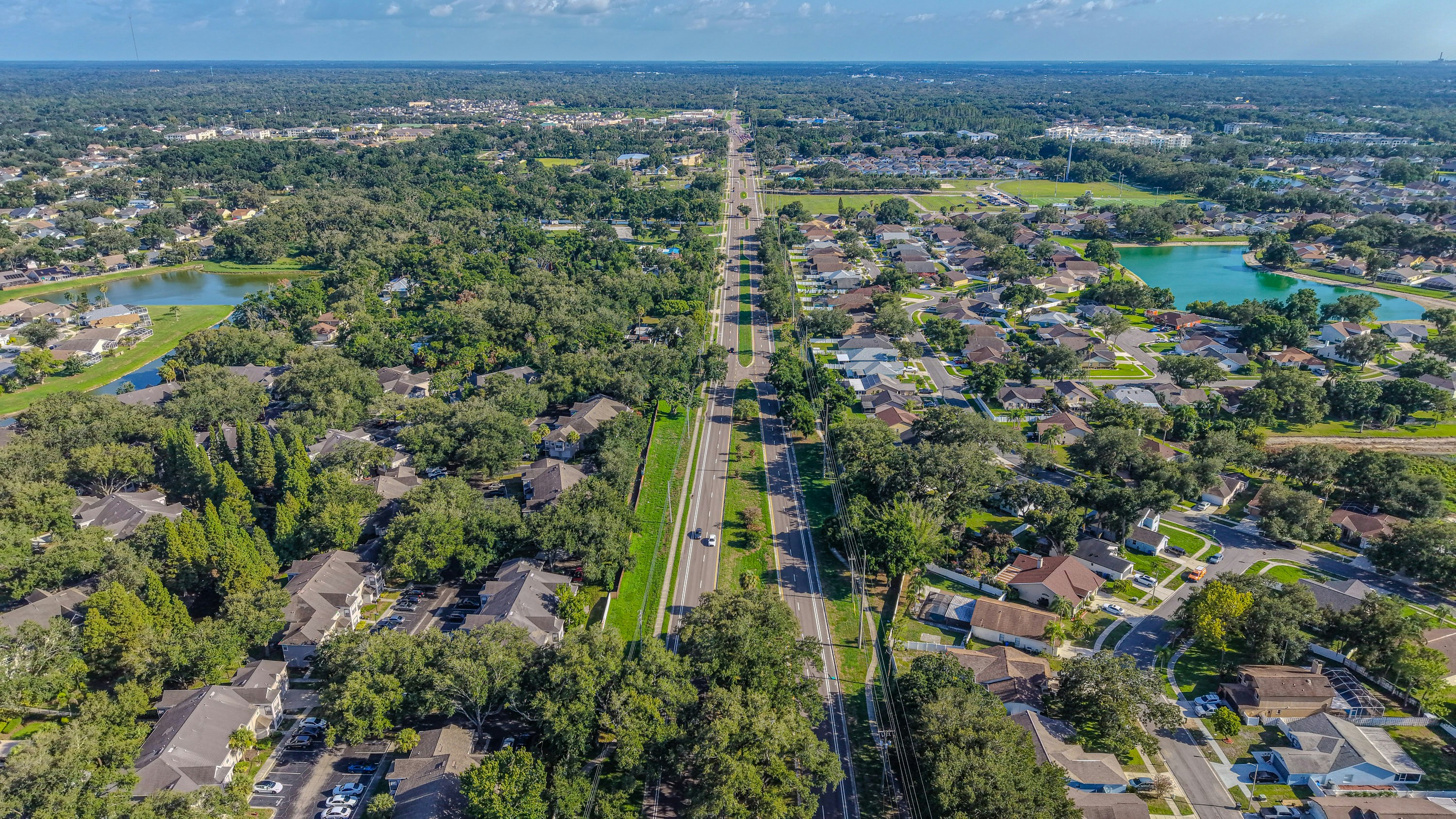 Long road through suburban landscape with houses, trees, and lakes
