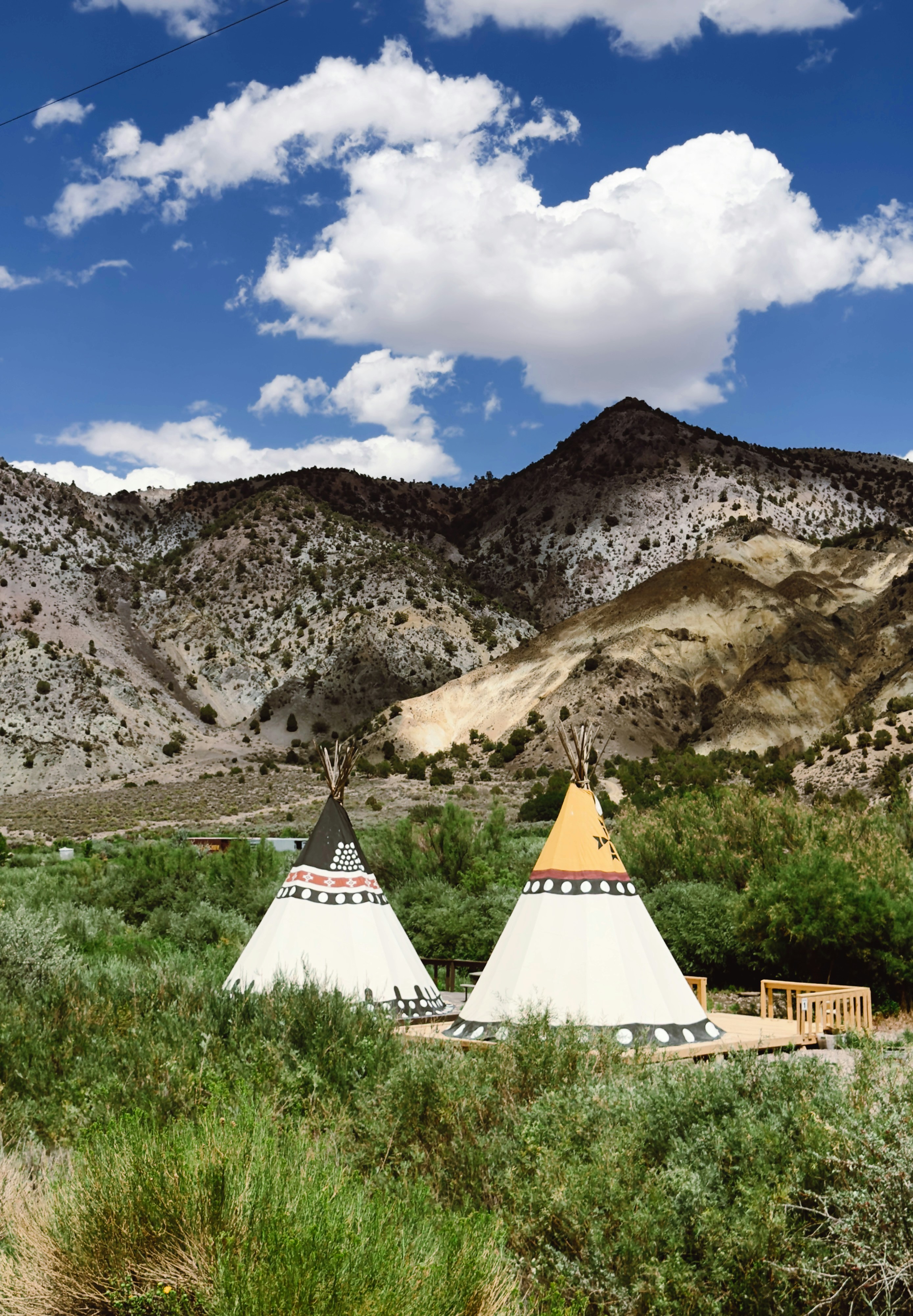 Two decorated tipis in a green valley beneath mountains